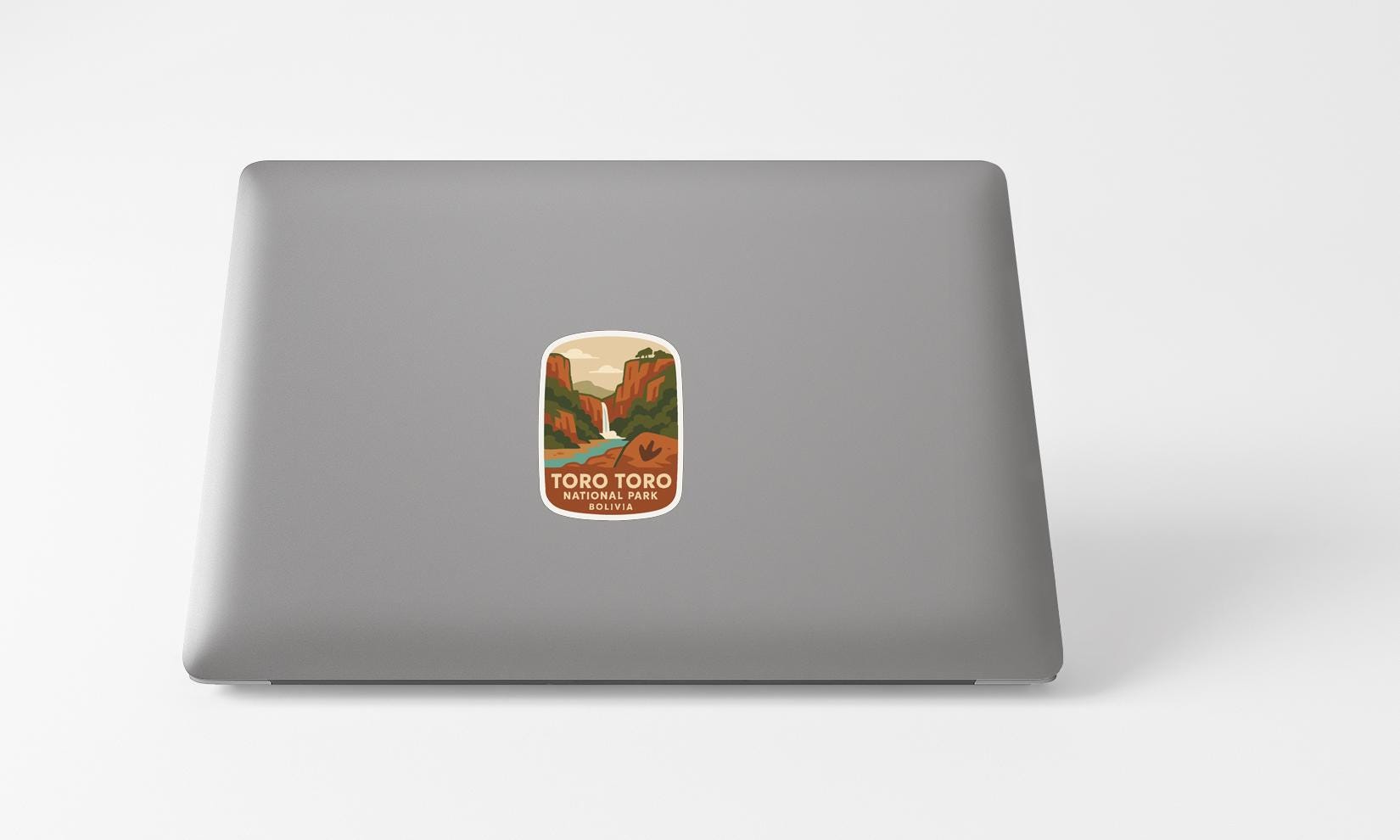A sticker with a mountain landscape and a river is placed on the back of a laptop computer.