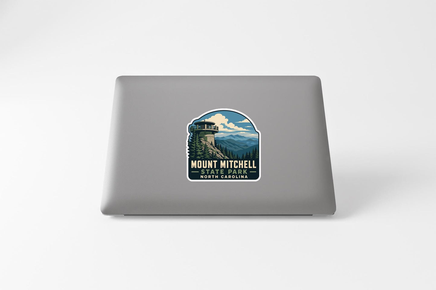 A sticker on the back of a laptop, depicting a scenic mountain landscape with a tower in the background.