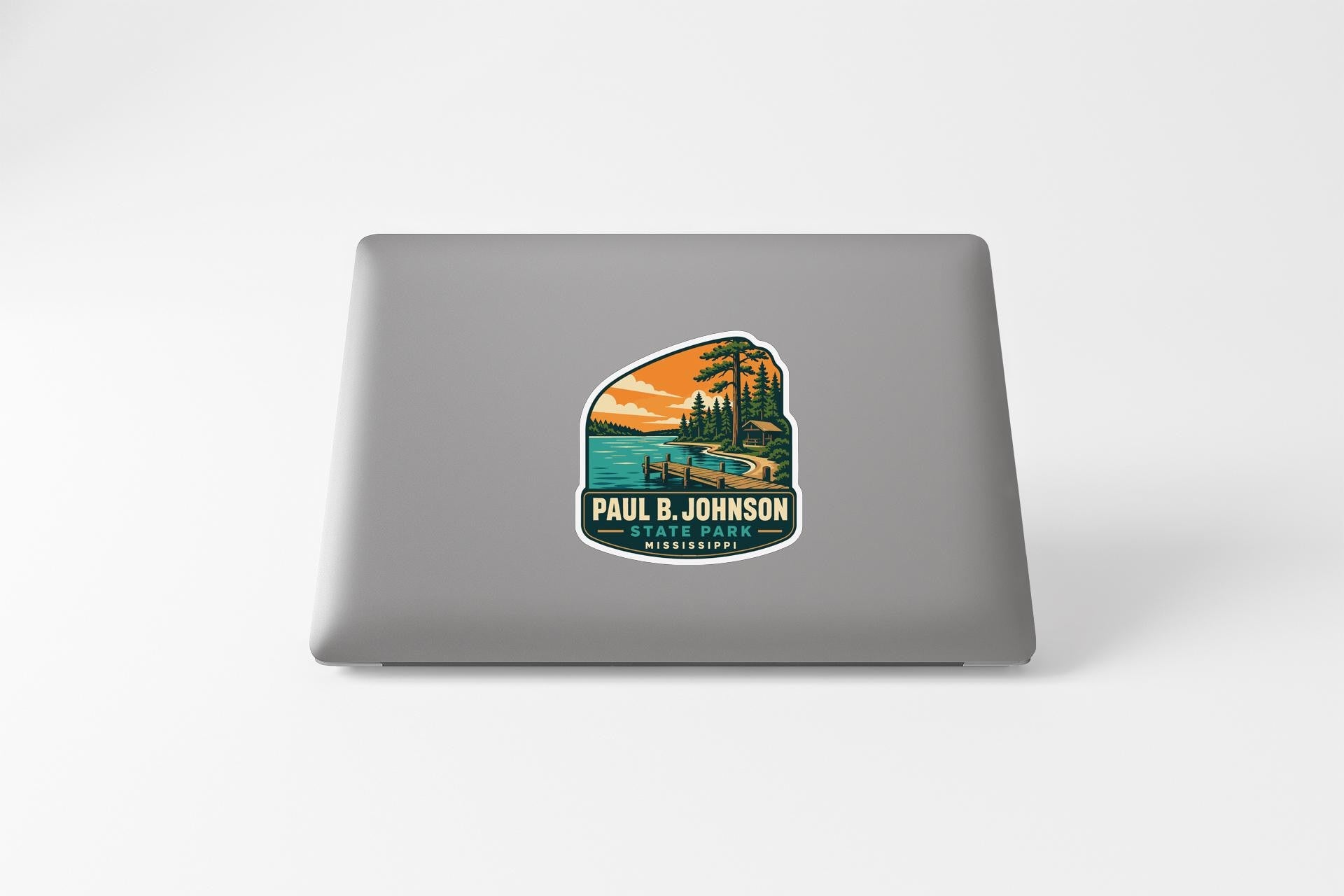 A sticker on the back of a laptop, depicting a scenic landscape with a lake, mountains, and trees.