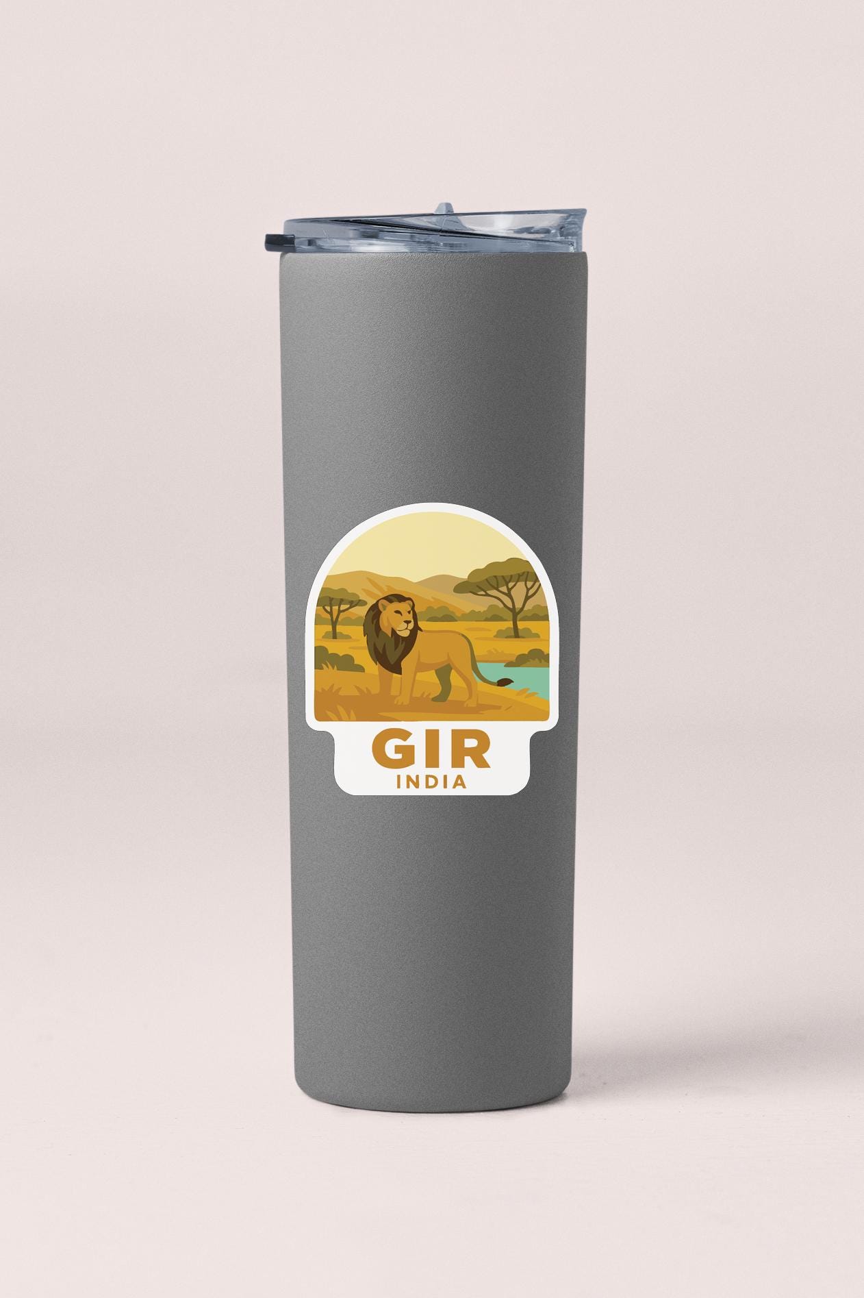 A gray tumbler with a sticker depicting a lion in a savanna landscape and the text "GIR INDIA" below it.