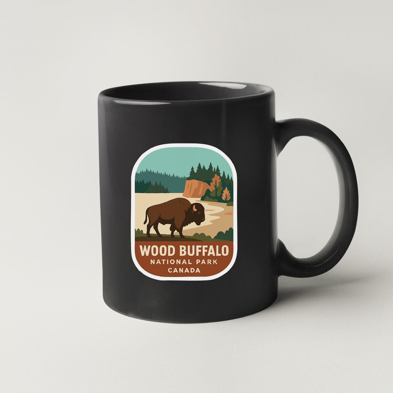 A black coffee mug with a label that features an illustration of a bison in a natural setting, along with the text "WOOD BISON NATIONAL PARK CANADA".