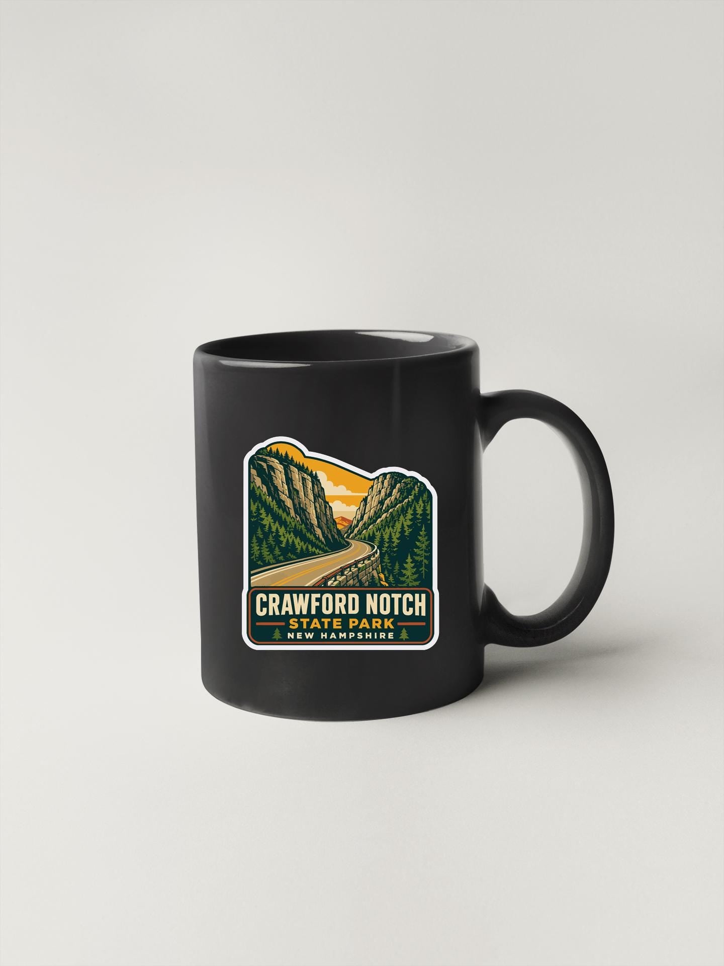 A black coffee mug with a sticker depicting a scenic mountain landscape.
