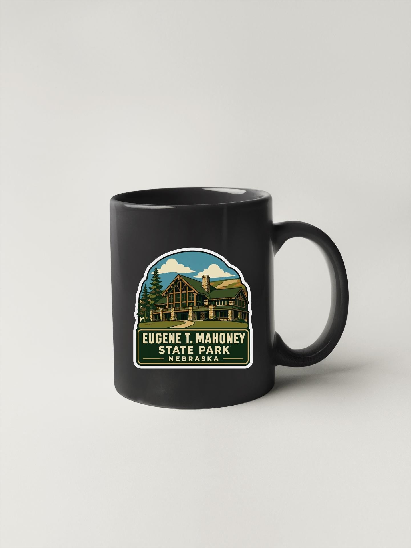 A black coffee mug with a sticker depicting a cabin and the text "Eugene T. Mahoney State Park, Nebraska" printed on it.