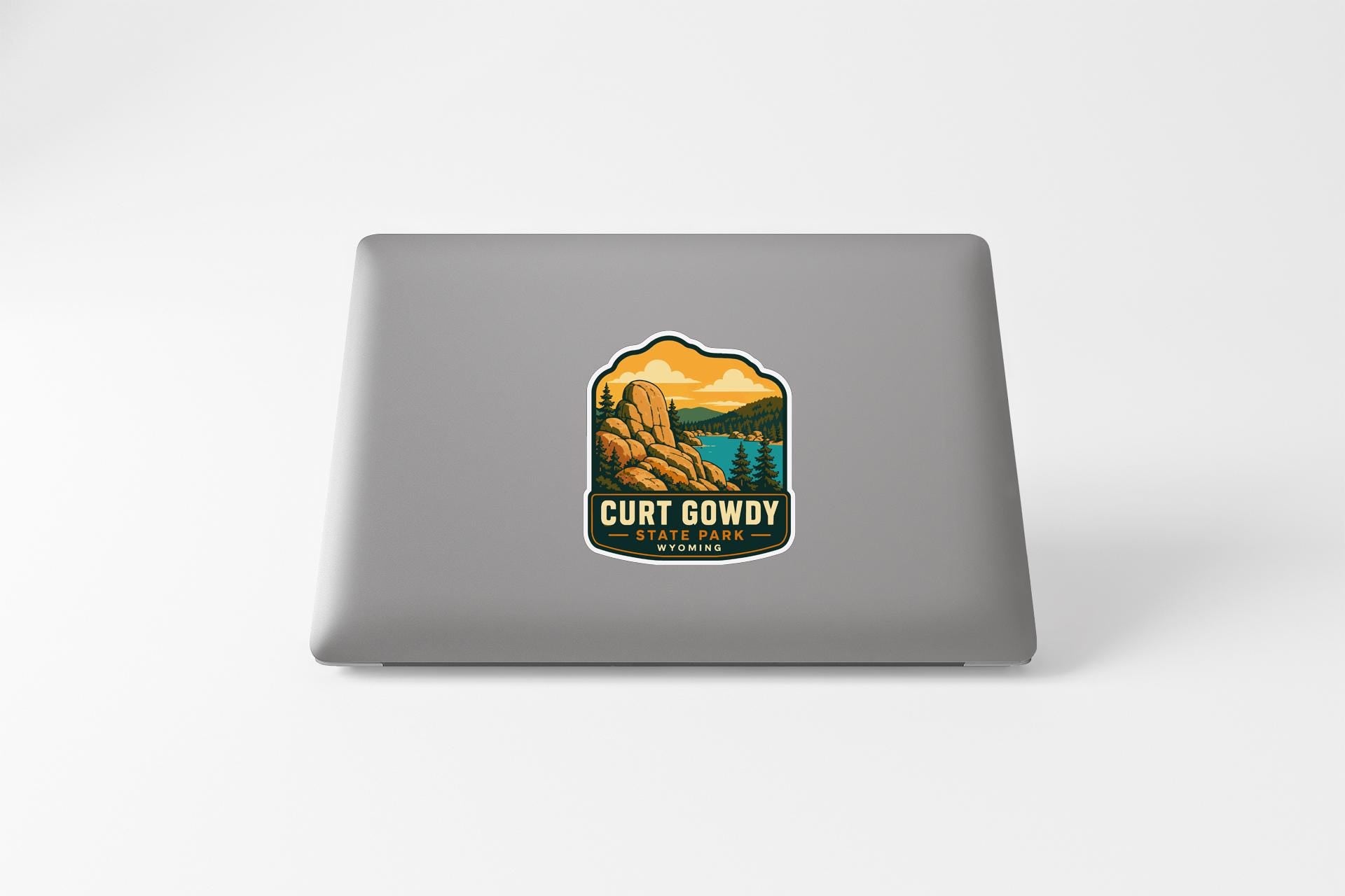 A sticker on the back of a laptop that features a mountain landscape with a lake and trees.