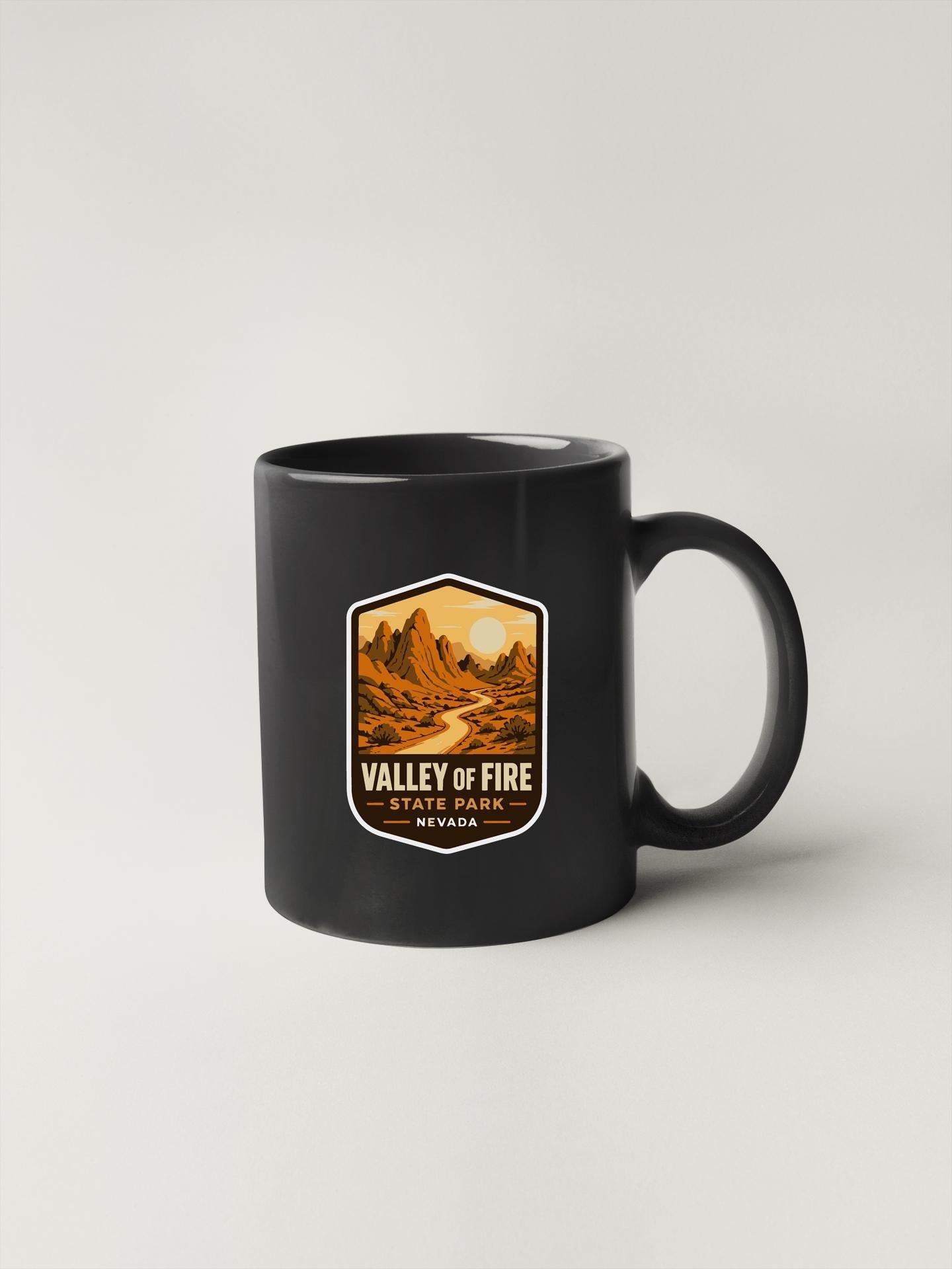 A black coffee mug with a graphic design depicting a scenic landscape, including mountains, a river, and a sun.