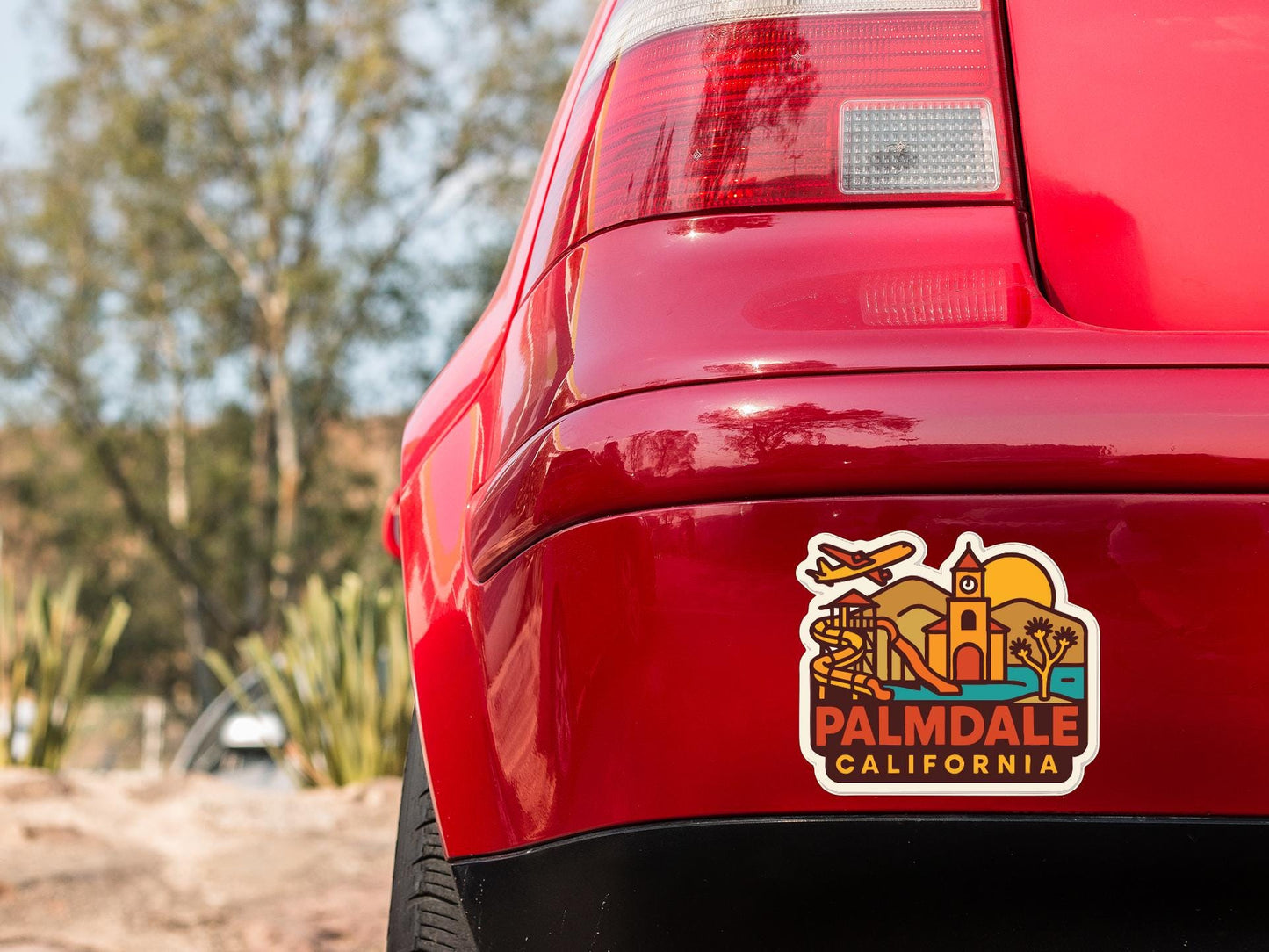 the rear end of a red car with a sticker on the trunk that says "Palmdale, California".