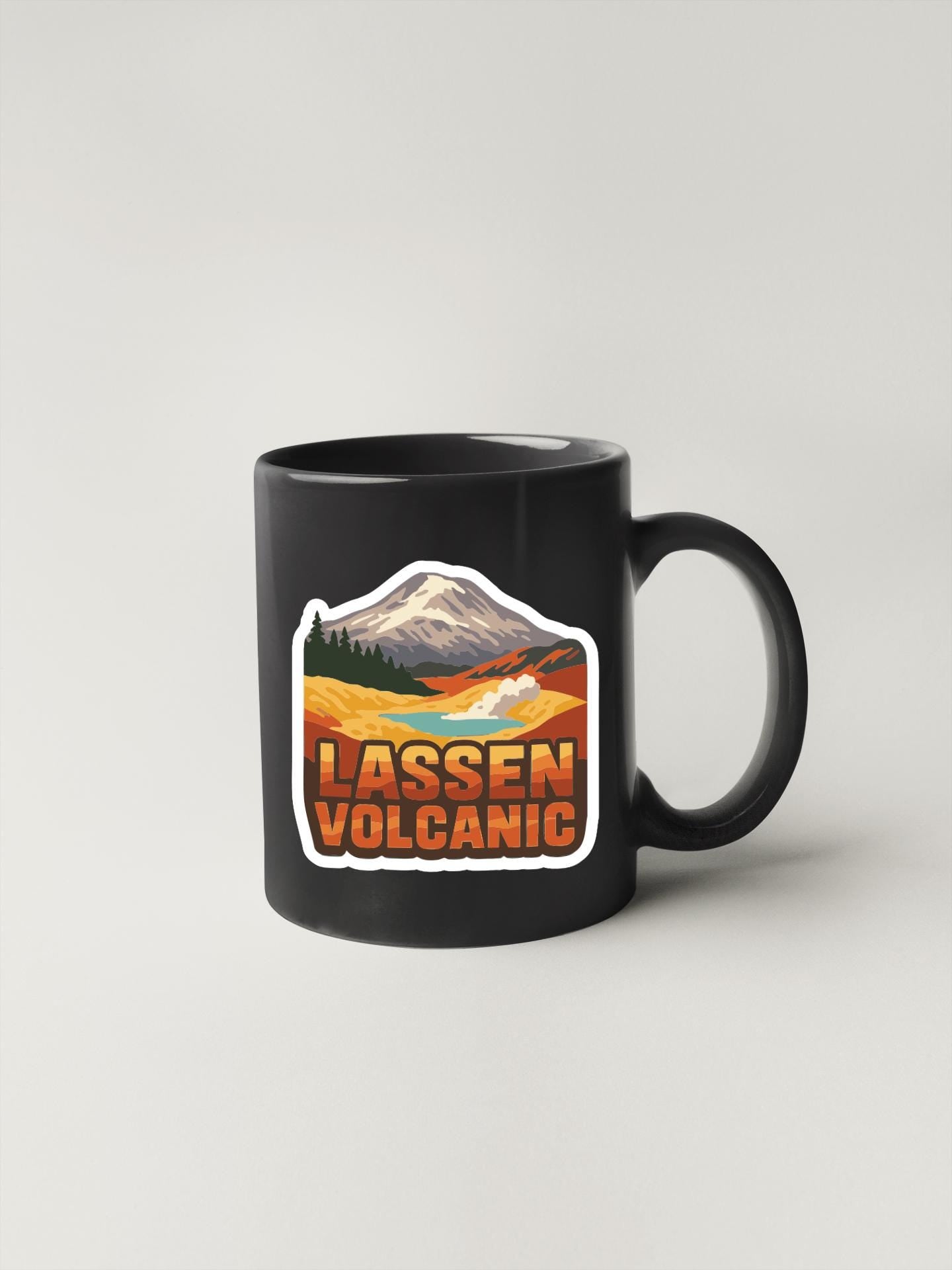 A black coffee mug with a sticker depicting a mountain landscape and the text "LASSEN VOLCANIC".