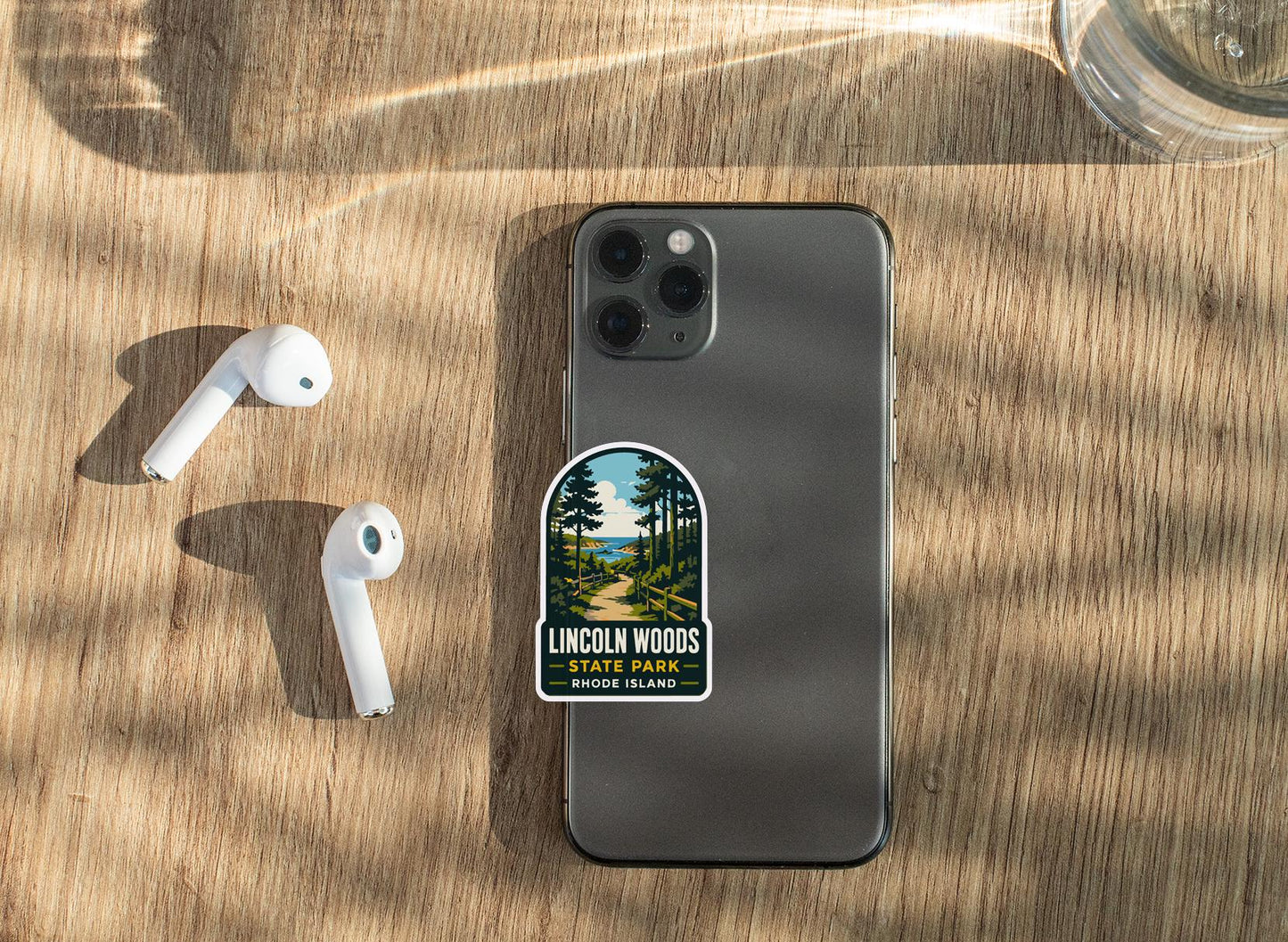 a smartphone with a sticker on it, placed on a wooden surface alongside a pair of white earbuds.