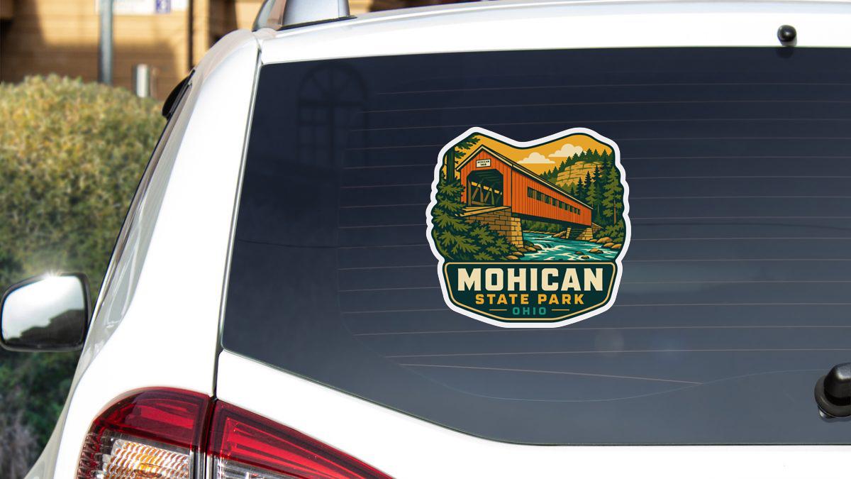 A sticker on the rear window of a vehicle, depicting a scenic landscape with a bridge and trees, indicating Mohican State Park in Ohio.
