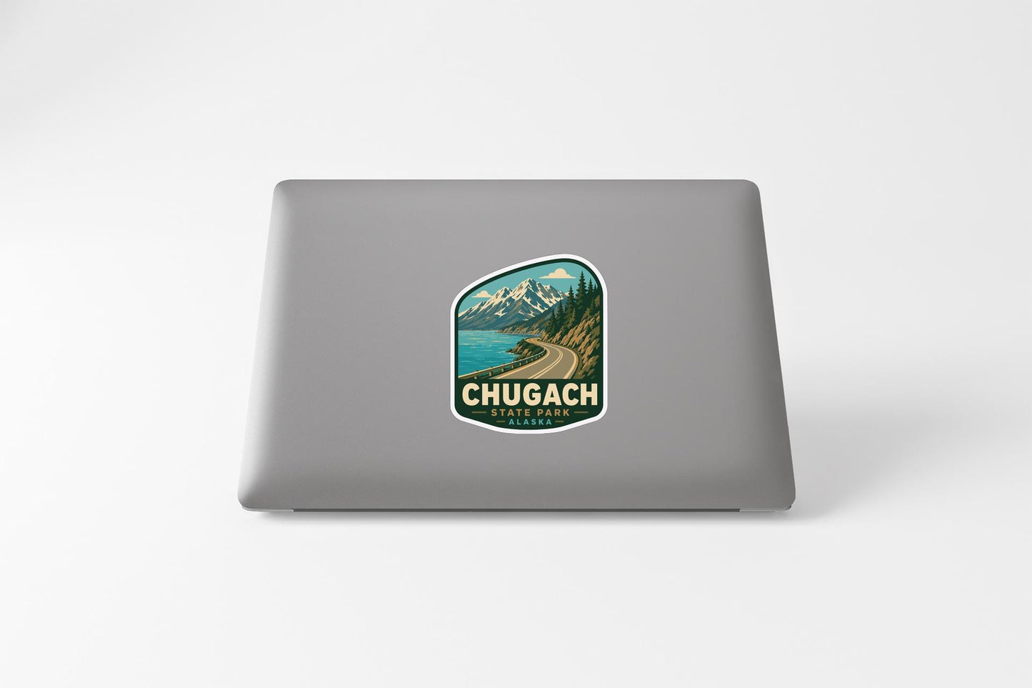A sticker on the back of a laptop, depicting a scenic mountain landscape with a winding road and a body of water.
