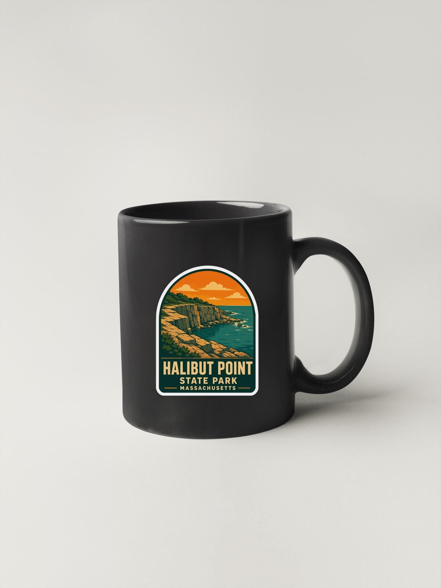 A black coffee mug with a graphic design depicting a coastal landscape, featuring the text "HALIBUT POINT STATE PARK MASSACHUSETTS".