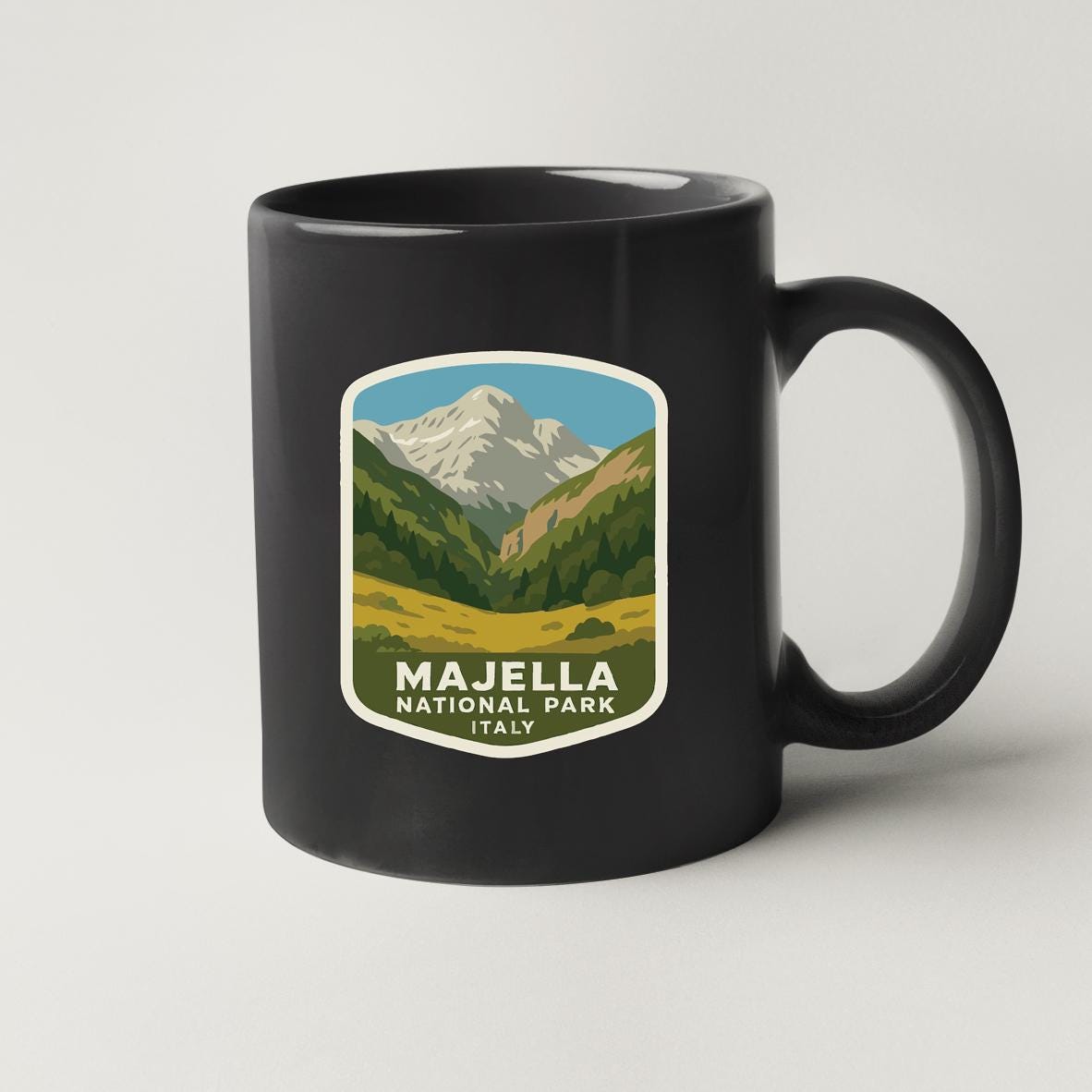 A black coffee mug with a graphic design depicting a mountainous landscape and the text "MAJELLA NATIONAL PARK ITALY".