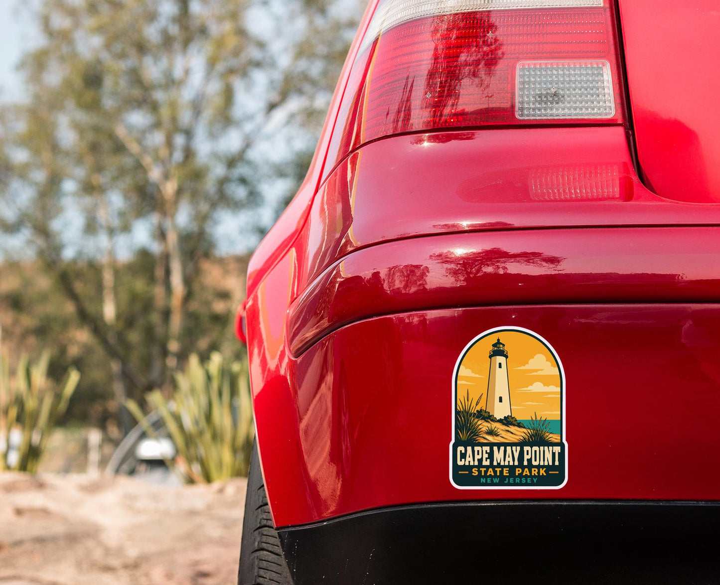 the rear end of a red car with a Cape May Point State Park sticker on the trunk.