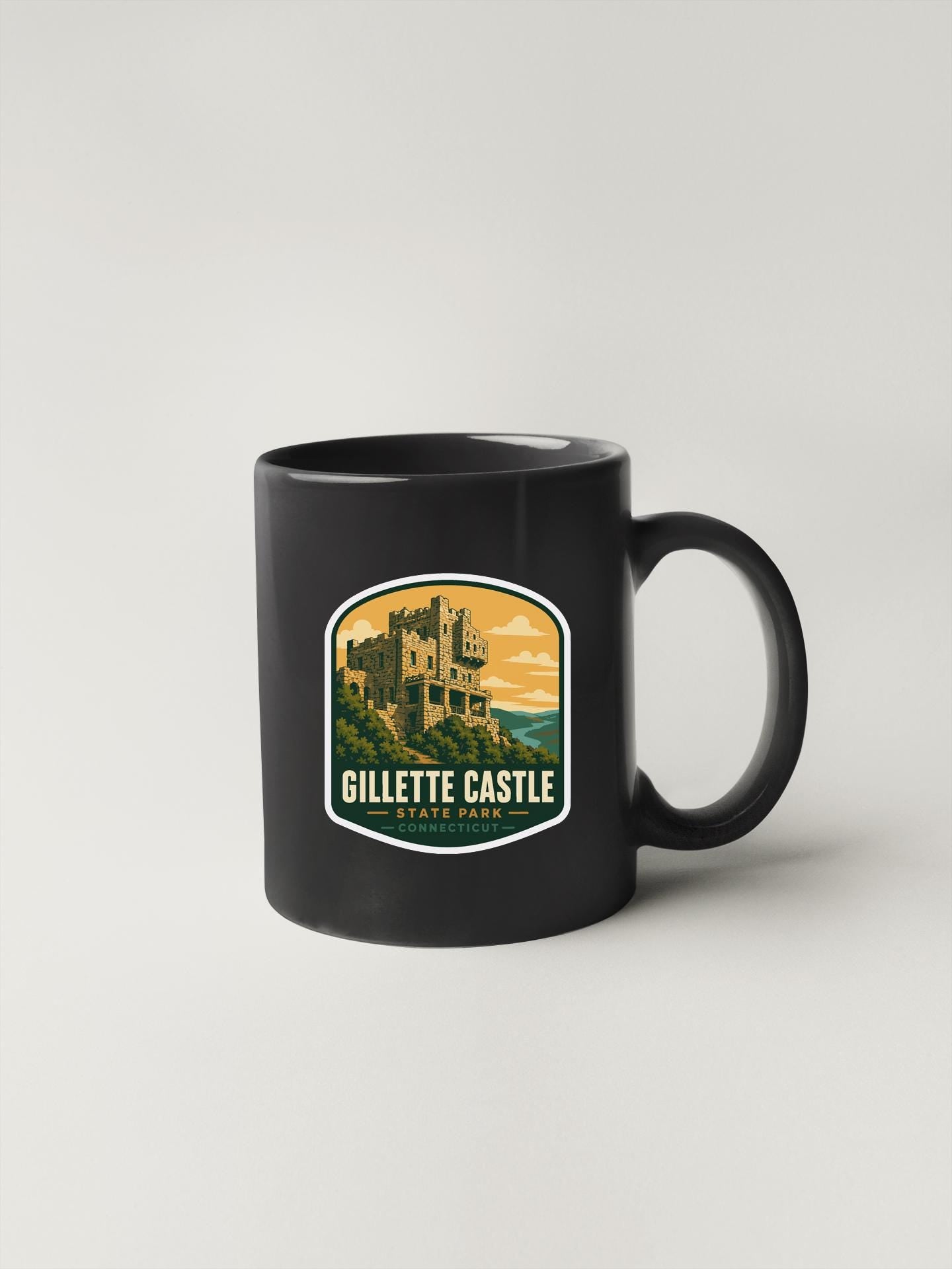 A black coffee mug with a graphic design depicting a castle or palace-like structure, along with the text "GILLETTE CASTLE STATE PARK".