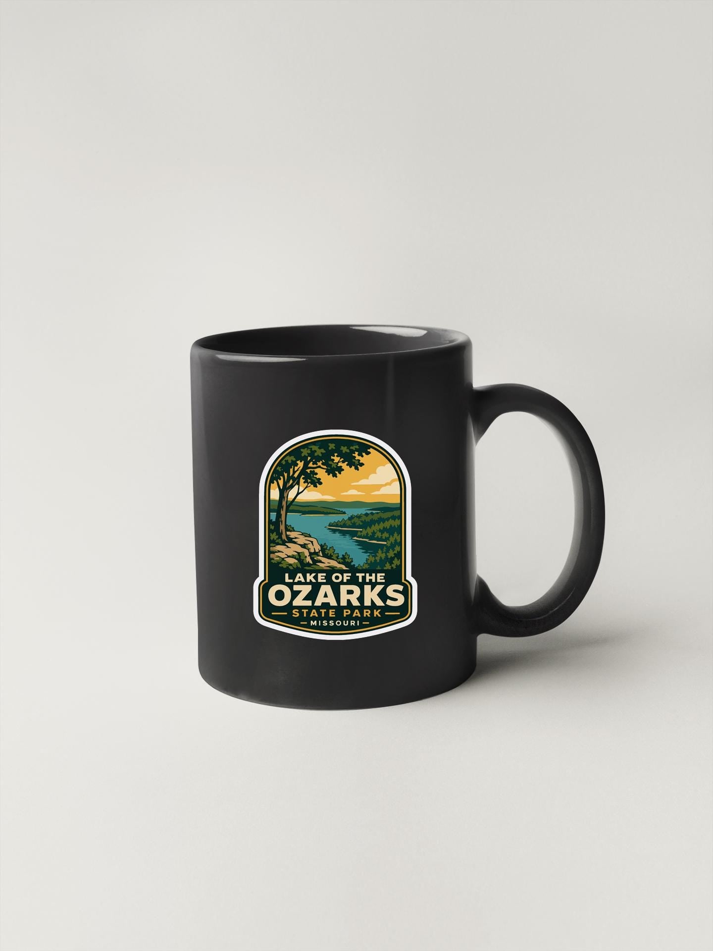 A black coffee mug with a label that says "Lake of the Ozarks" and features an illustration of a scenic landscape.
