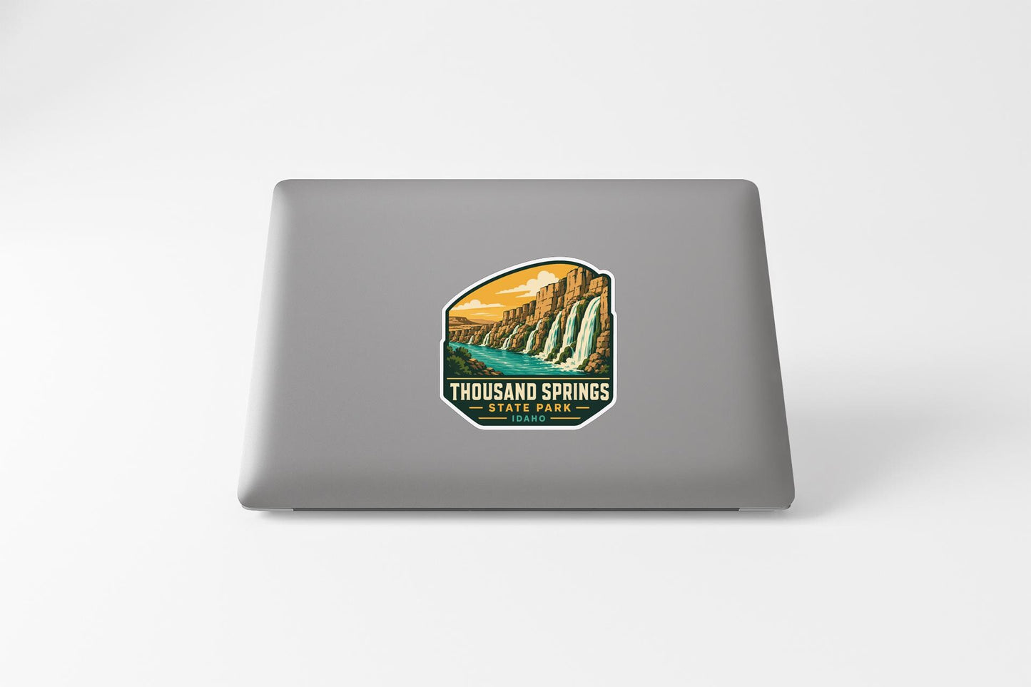 a sticker on the back of a laptop that displays a scenic landscape with a waterfall and a river.