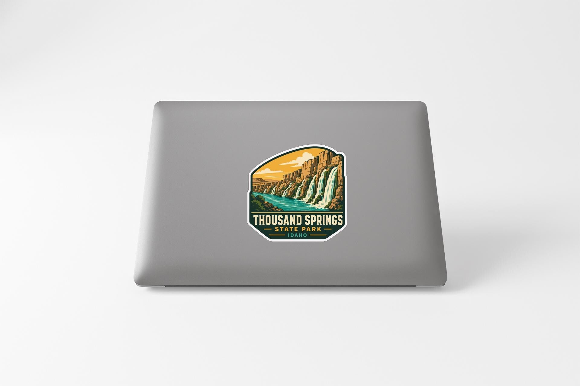 a sticker on the back of a laptop that displays a scenic landscape with a waterfall and a river.