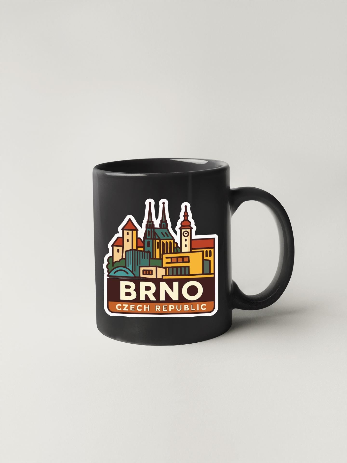 A black coffee mug with a colorful illustration of the city of Brno, Czech Republic, featuring buildings and landmarks.