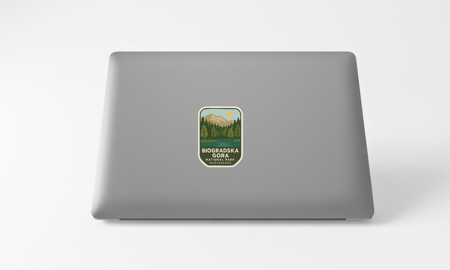A sticker on the back of a laptop, depicting a mountain landscape with a lake and trees.