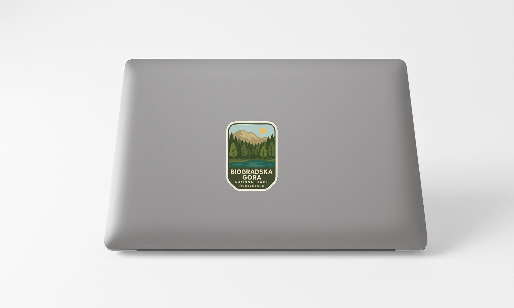 A sticker on the back of a laptop, depicting a mountain landscape with a lake and trees.