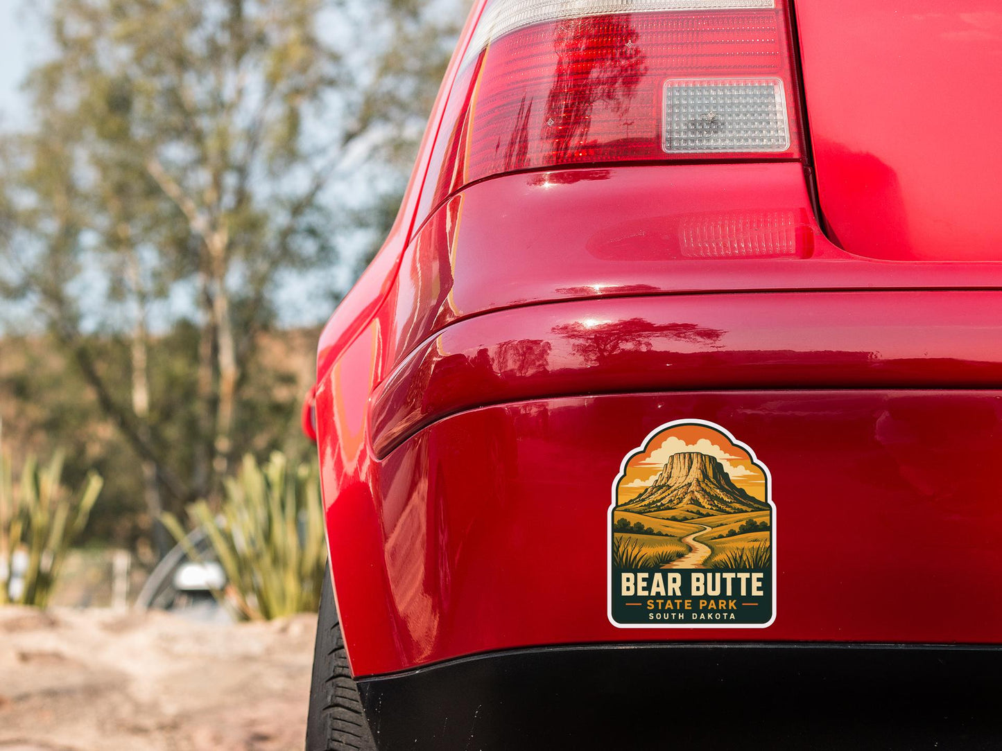 the rear end of a red car with a sticker on the back window that reads "BEAR BUTTE STATE PARK SOUTH DAKOTA".