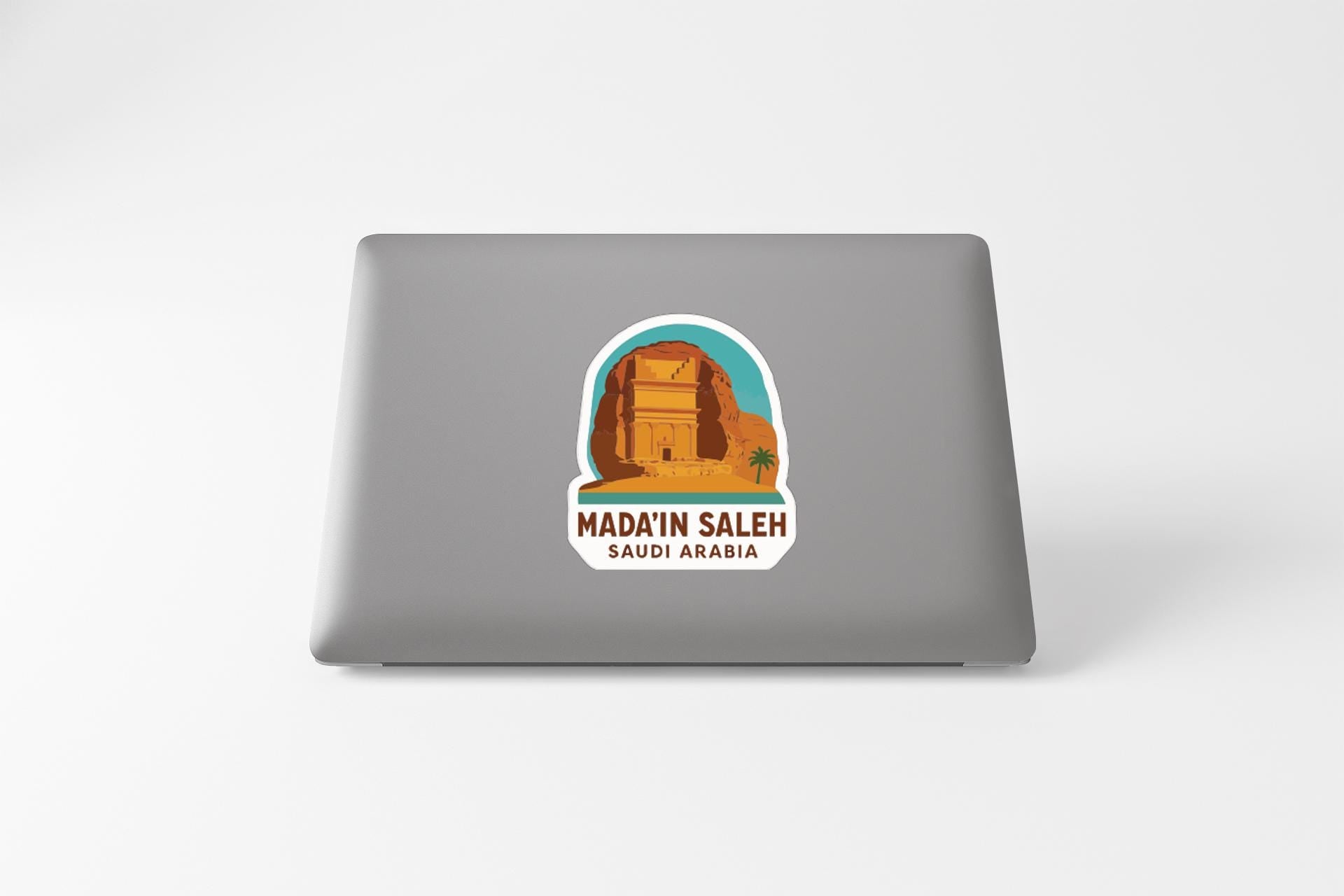 a sticker with an illustration of a desert landscape and the text "MADIN SALEH SAUDI ARABIA" printed on a laptop.