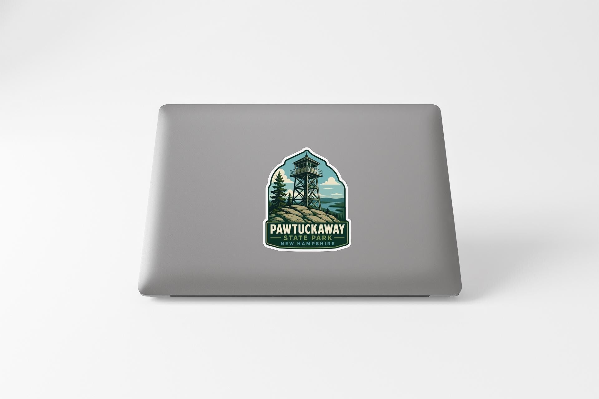 A sticker on the back of a laptop, depicting a tower or observation tower surrounded by trees and mountains, with the text "PAWTUCKAWAY TUNNEL PARK" below it.