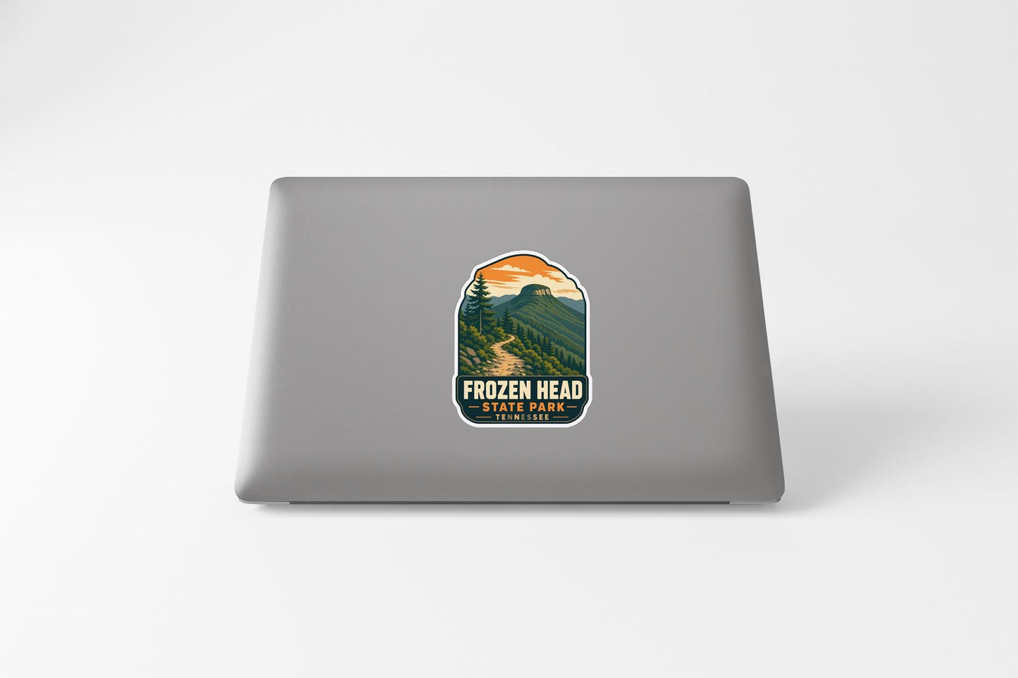 A sticker on the back of a laptop, depicting a scenic mountain landscape with a winding trail.