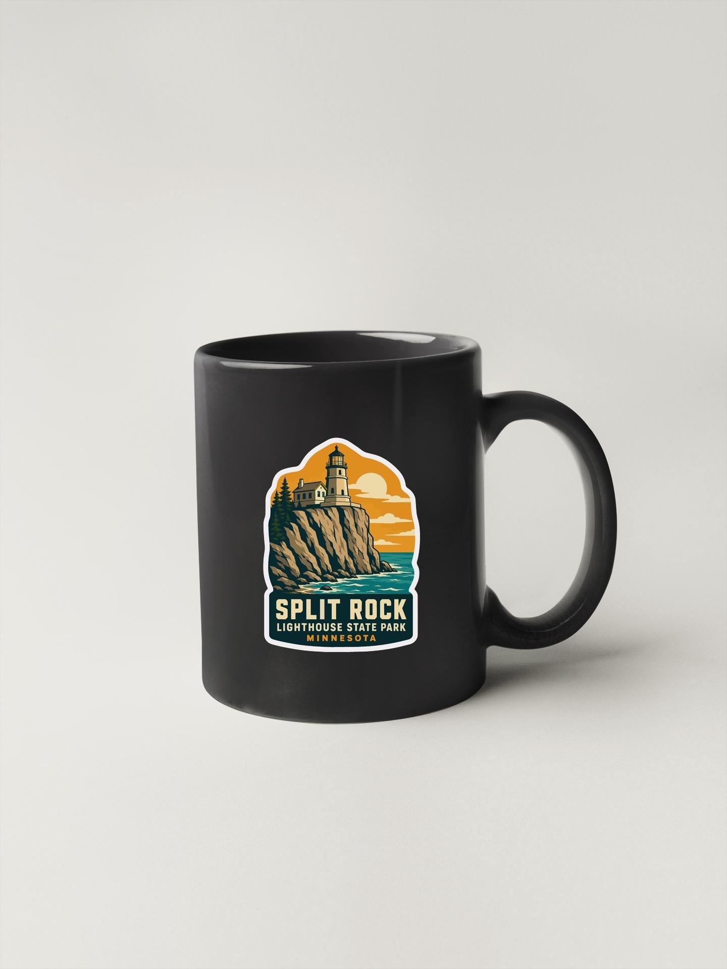 A black coffee mug with a graphic design depicting a lighthouse on a cliff, along with the text "SPLIT ROCK LIGHTHOUSE STATE PARK MINNESOTA".