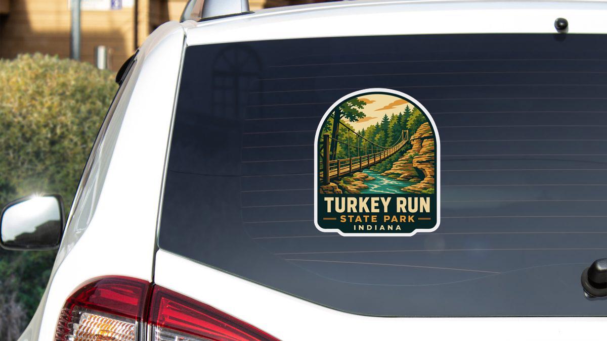 A sticker on the rear window of a white car, depicting a scenic landscape with a bridge and trees, advertising Turkey Run State Park in Indiana.