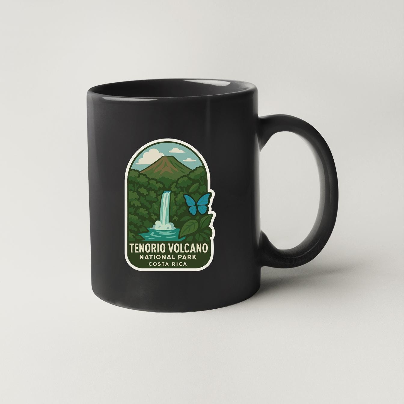 A black coffee mug with a label that says "TENORIO VOLCANO NATIONAL PARK COSTA RICA".