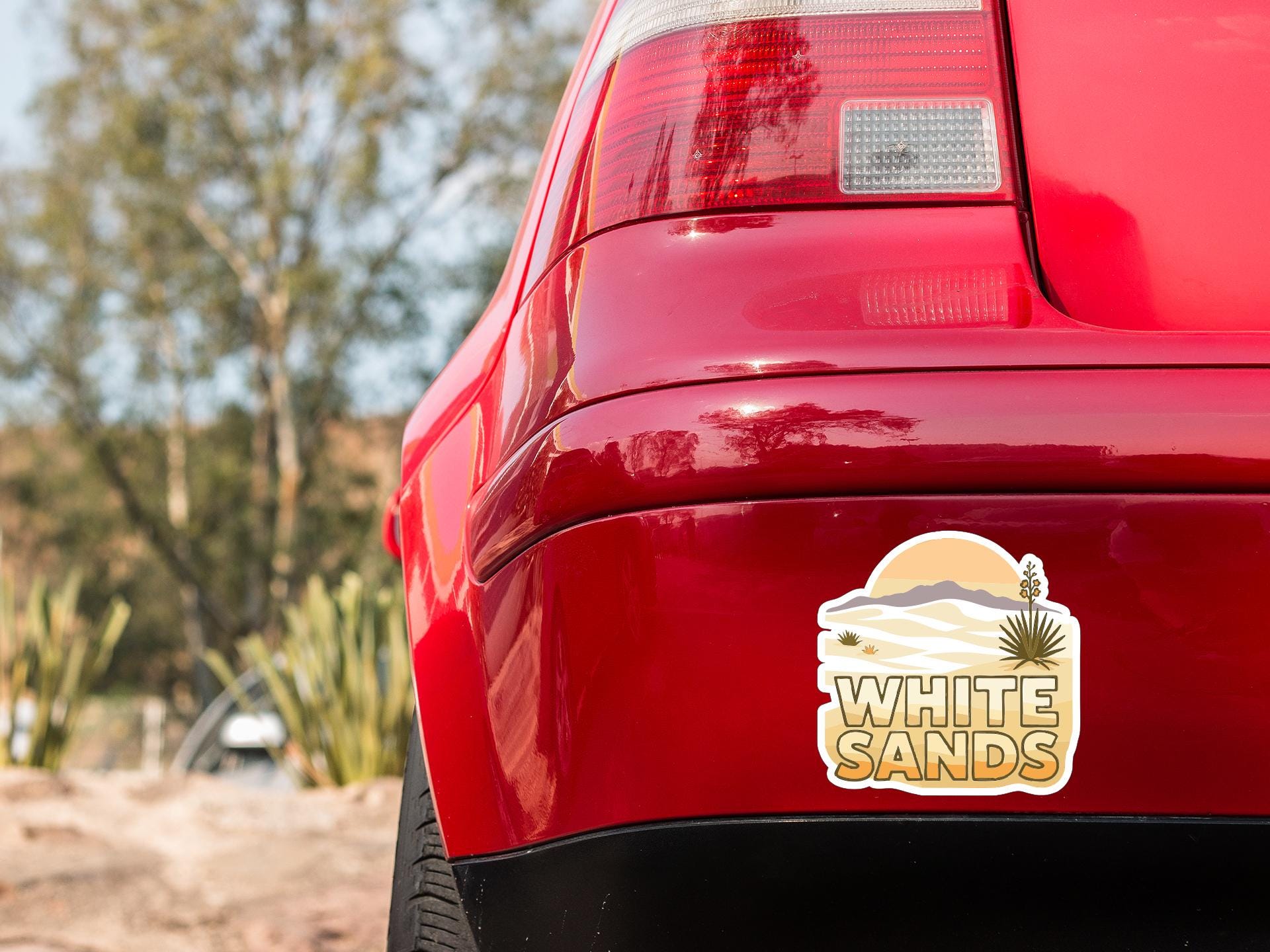 the rear end of a red car with a sticker on the trunk that says "WHITE SAND".