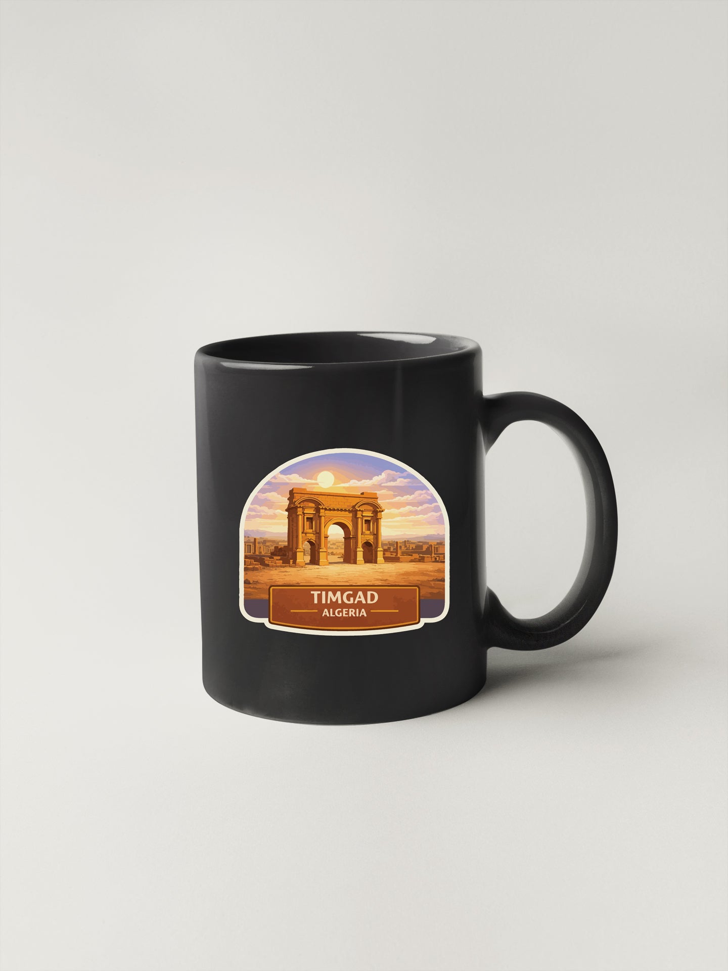 A black coffee mug with a sticker depicting the Timgad arch in Algeria.