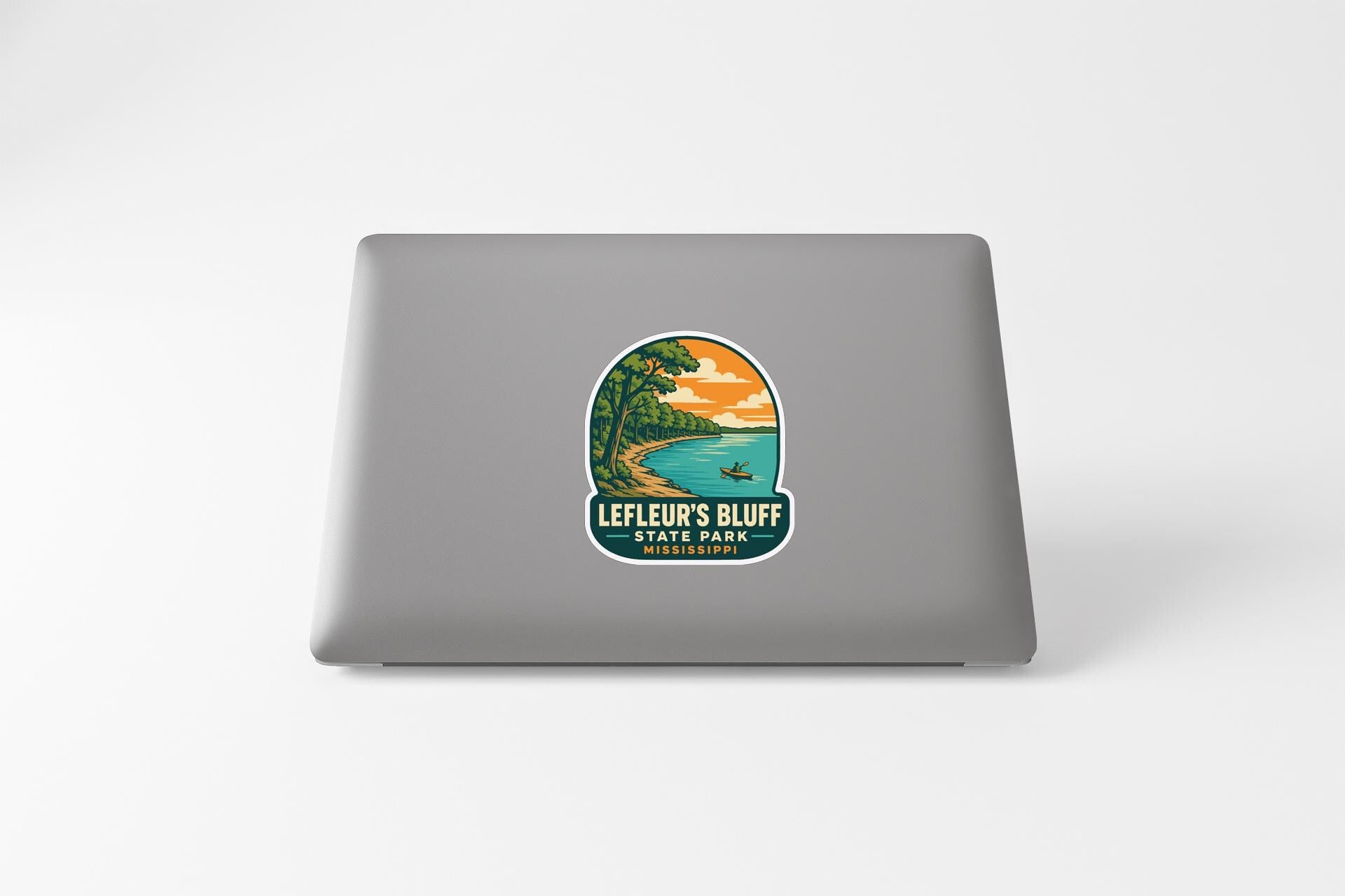 A sticker on the back of a laptop, depicting a scenic landscape with a lake, trees, and a sunset.
