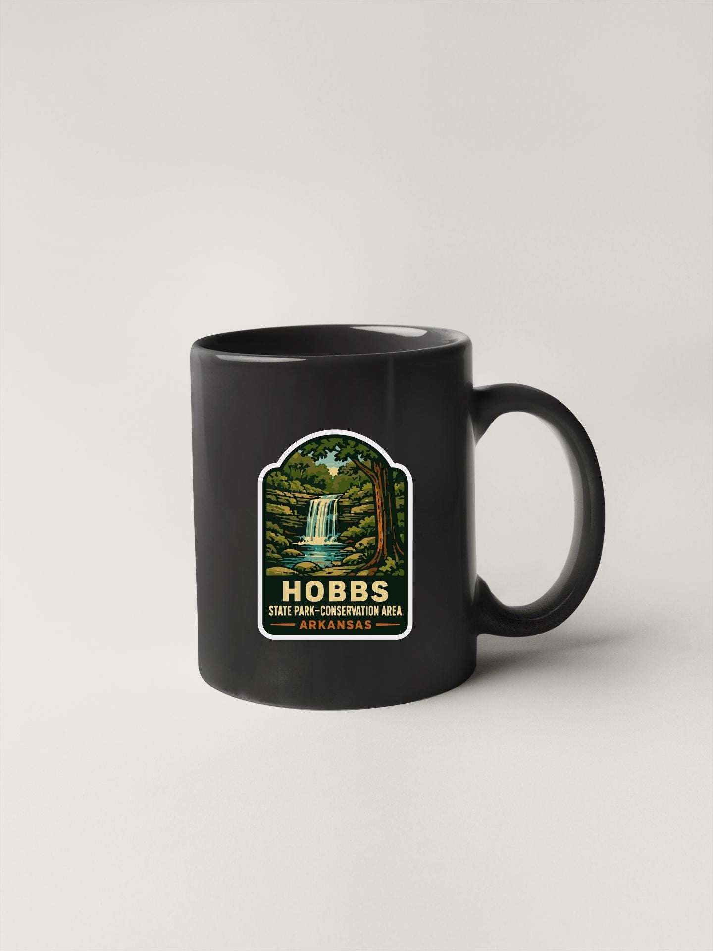 A black coffee mug with a sticker depicting a waterfall and forest.