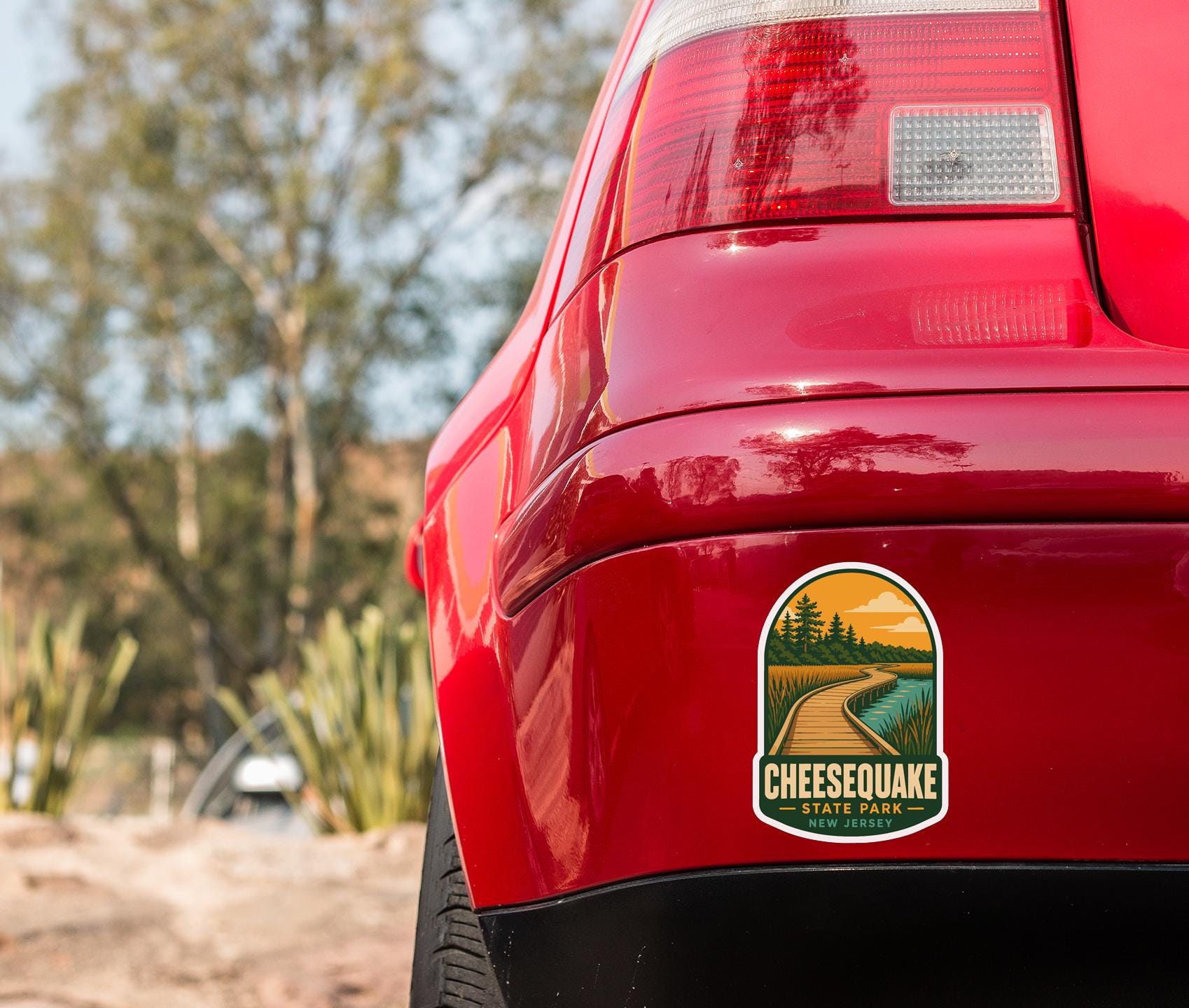 the rear end of a red car with a sticker on the back window that says "Cheesecake State Park, New Jersey".