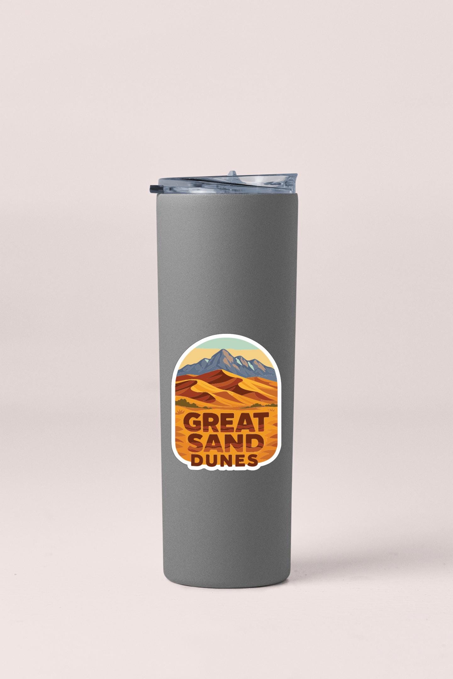 A gray insulated tumbler with a lid and a sticker featuring a desert landscape with mountains.