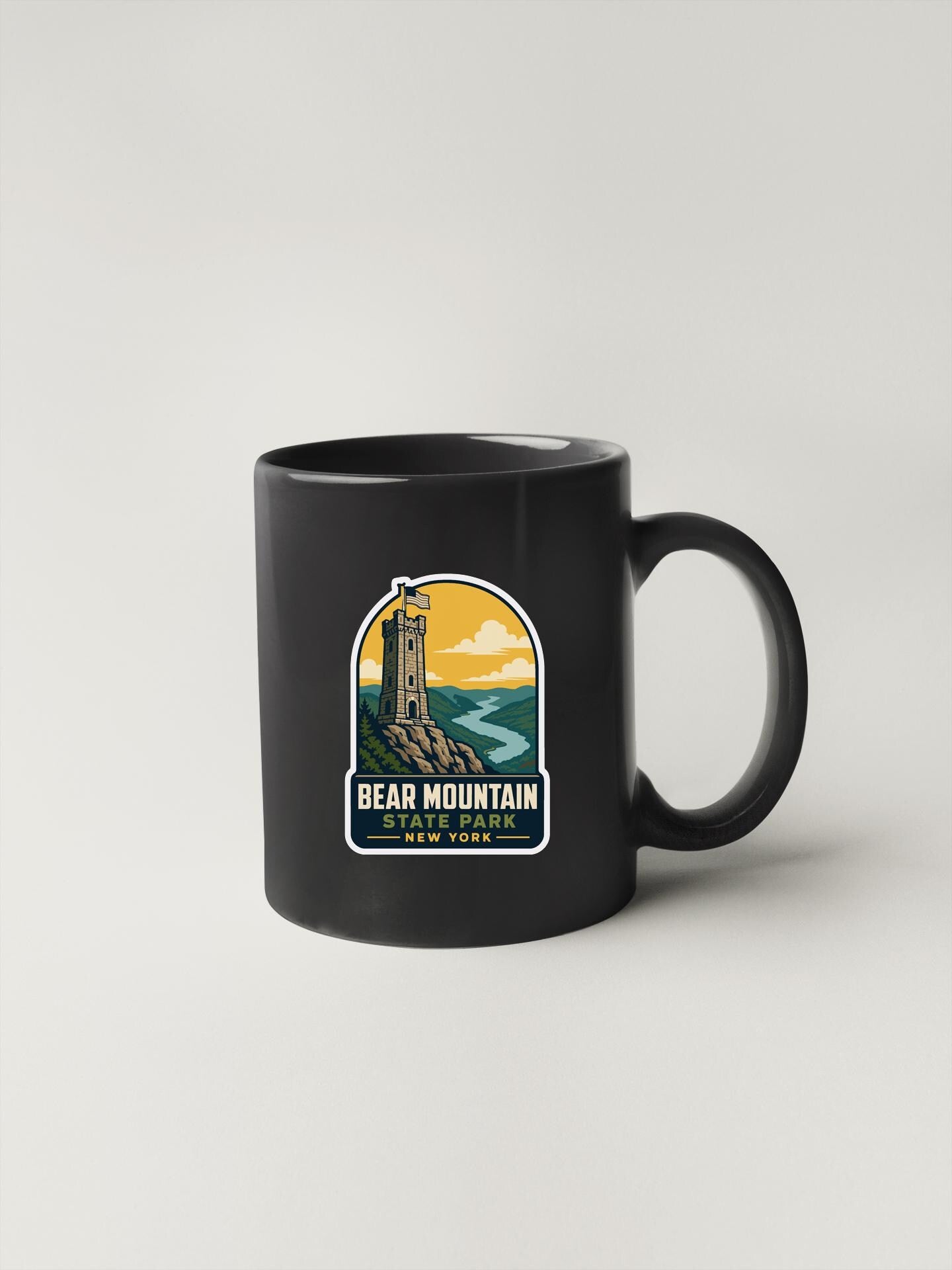 A black coffee mug with a sticker depicting Bear Mountain, a landmark in New York.