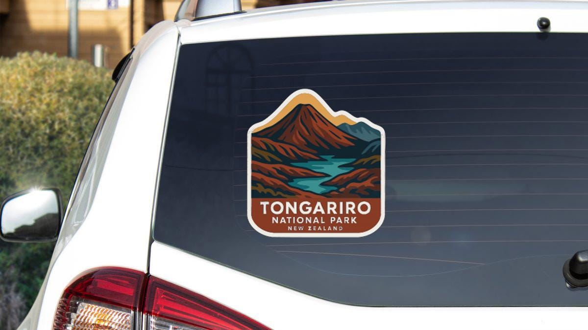 A sticker on the rear window of a car, depicting a scenic landscape with mountains and a lake, indicating Tongarro National Park in New Zealand.