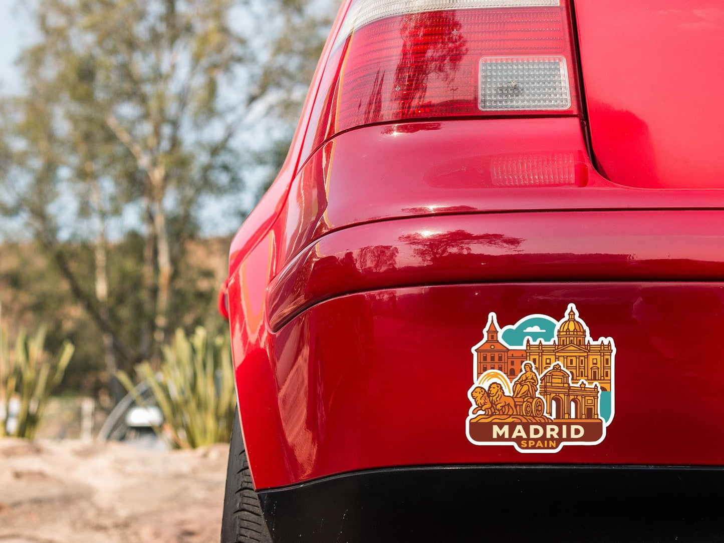 the rear end of a red car with a sticker on the trunk that features an illustration of a cityscape and the text "MADRID, SPAIN".