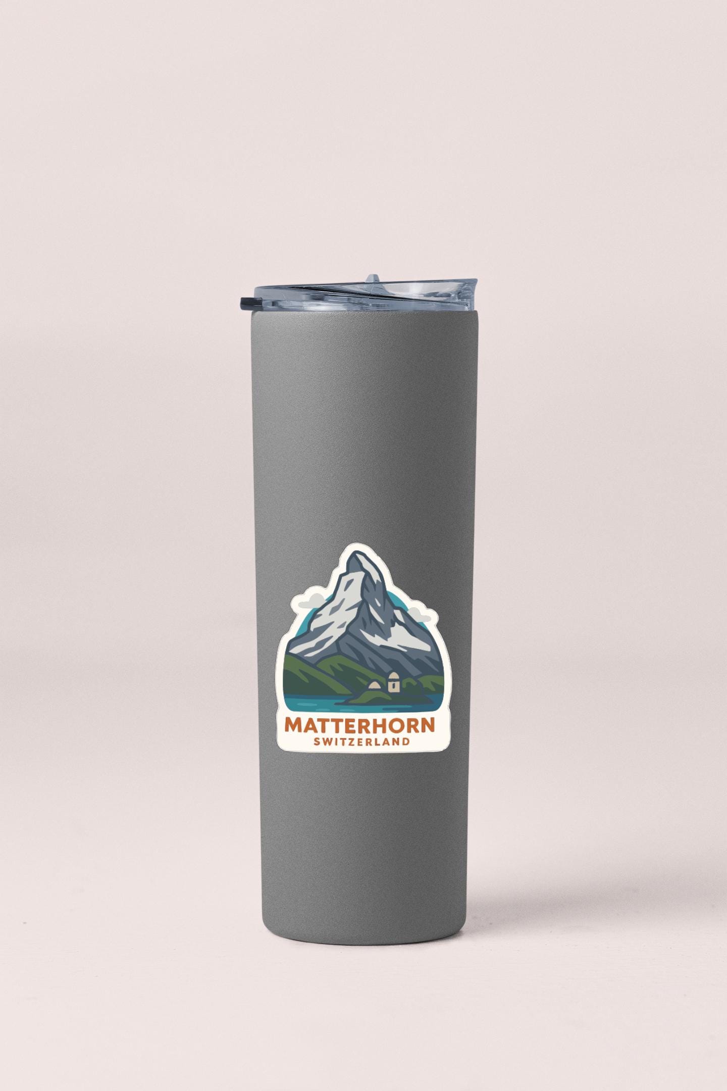 A gray insulated tumbler with a mountain sticker on it, representing the Matterhorn mountain in Switzerland.