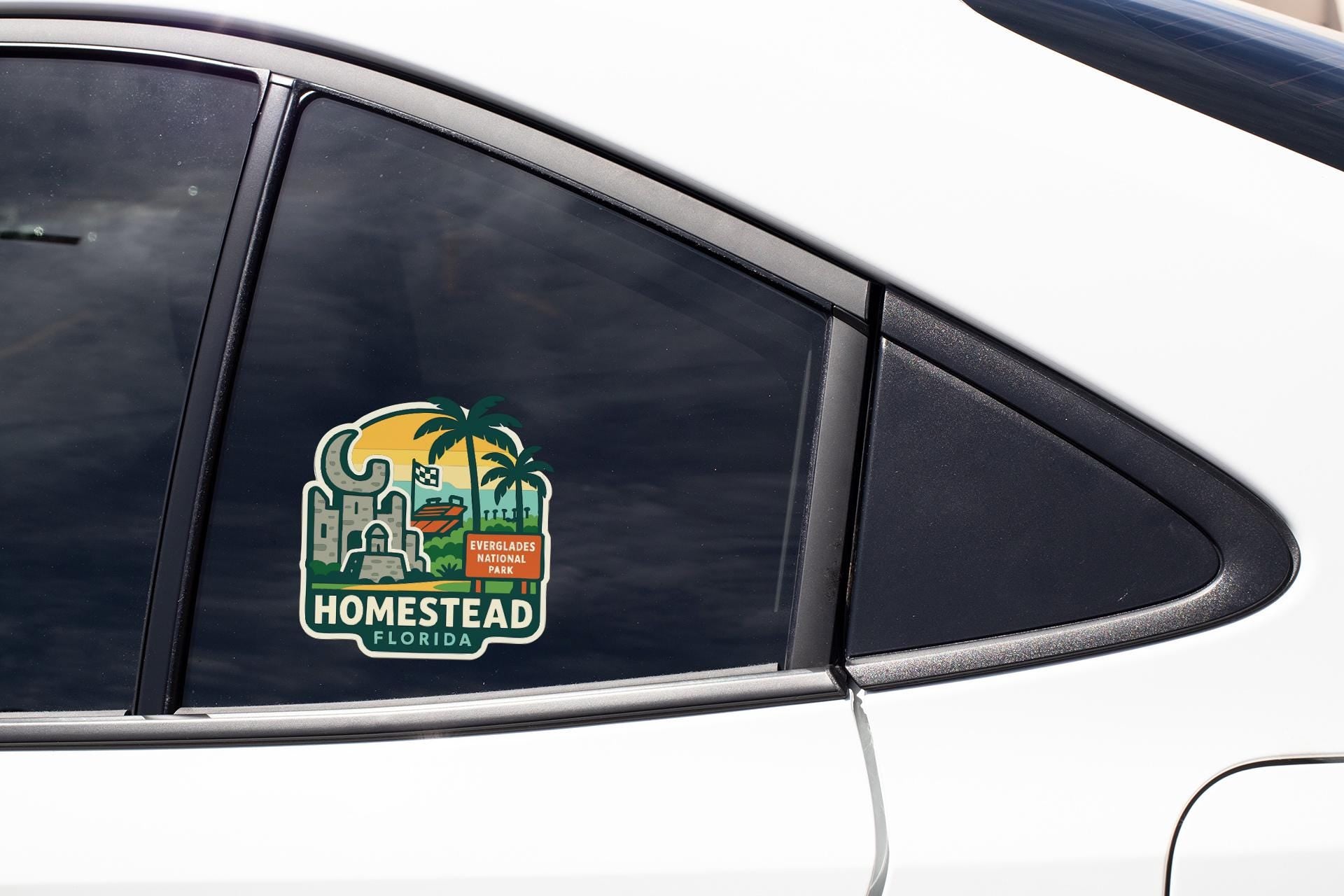 a sticker on the side of a car window, featuring a tropical landscape with palm trees and a building, along with the text "HOMESTAD FLORIDA" indicating the location.