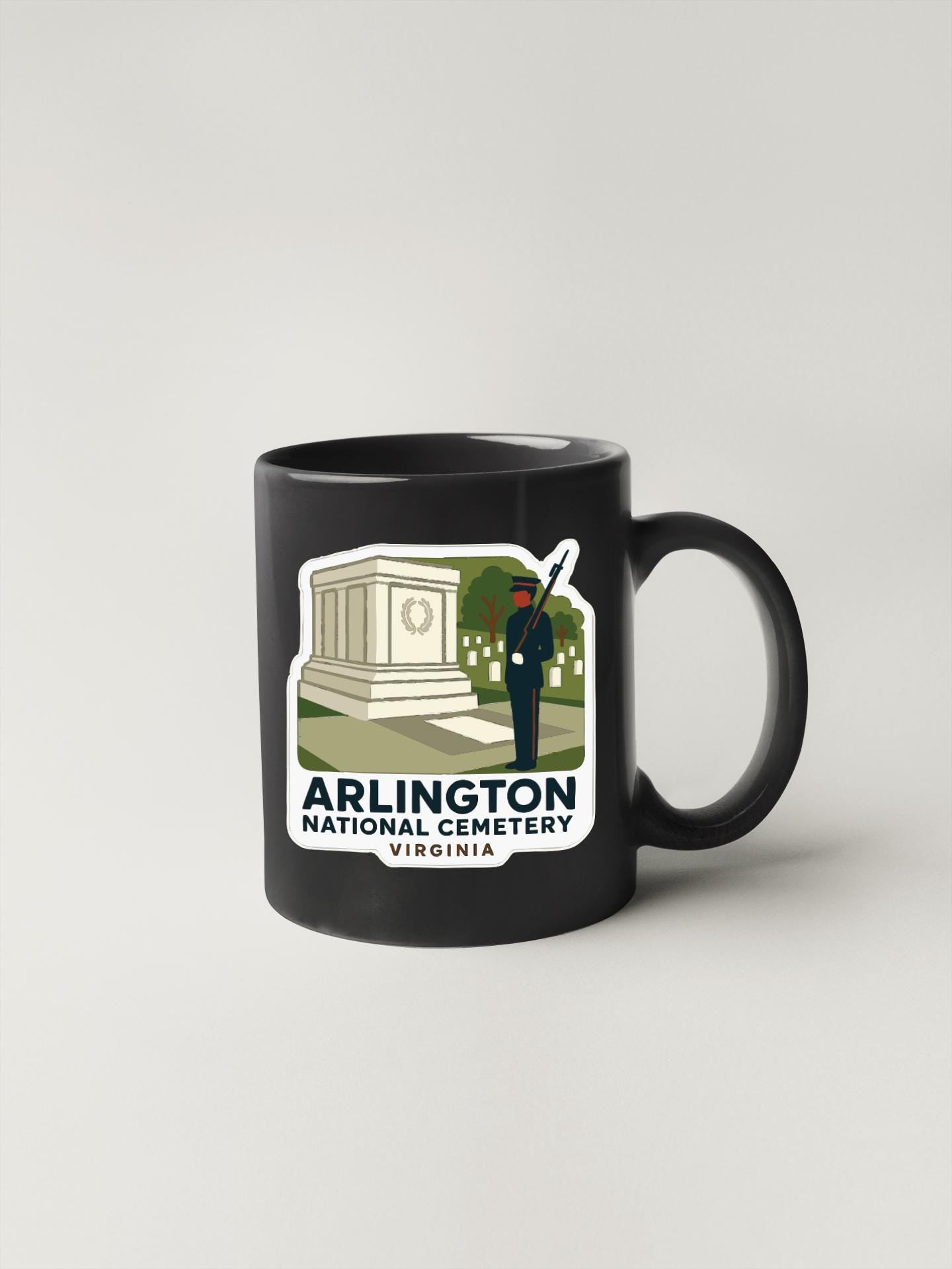 A black coffee mug with a sticker depicting the Arlington National Cemetery in Virginia.