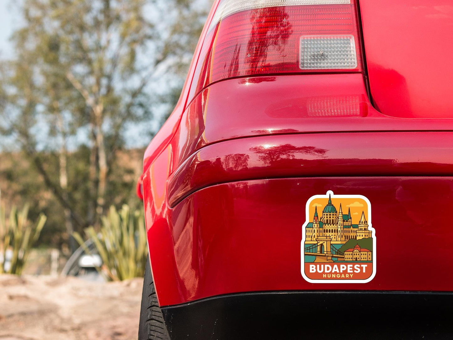 the rear end of a red car with a sticker on the trunk that features an illustration of the Hungarian capital city of Budapest.