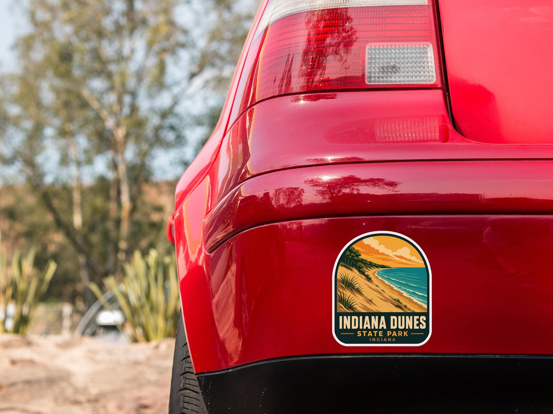 the rear end of a red car with a sticker on the back window that reads "Indiana Dunes State Park".