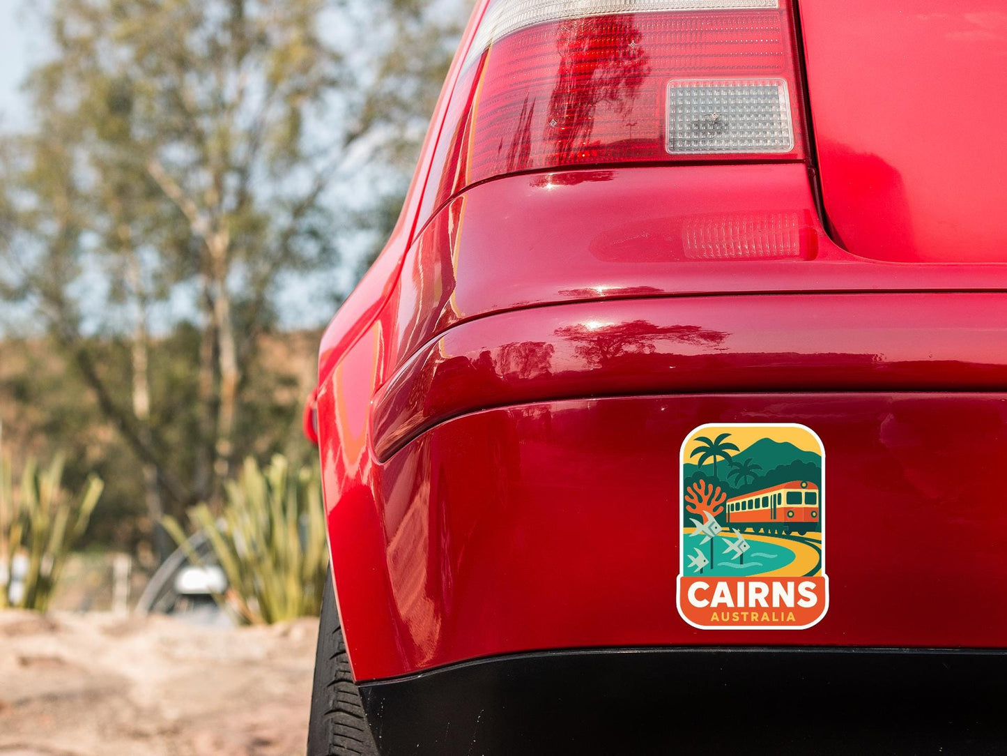 the rear end of a red car with a sticker on the back window that says "CAIRNS AUSTRALIA".