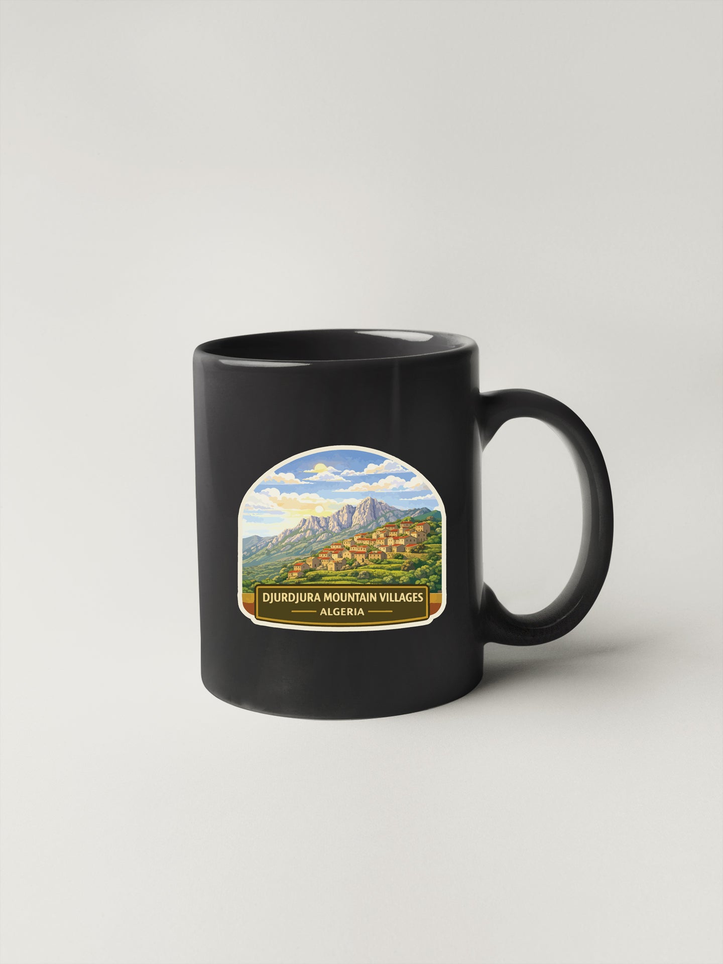 A black coffee mug with a label depicting a scenic mountain landscape and the text "DURJUJURA MOUNTAIN VILLAGES ALGERIA".