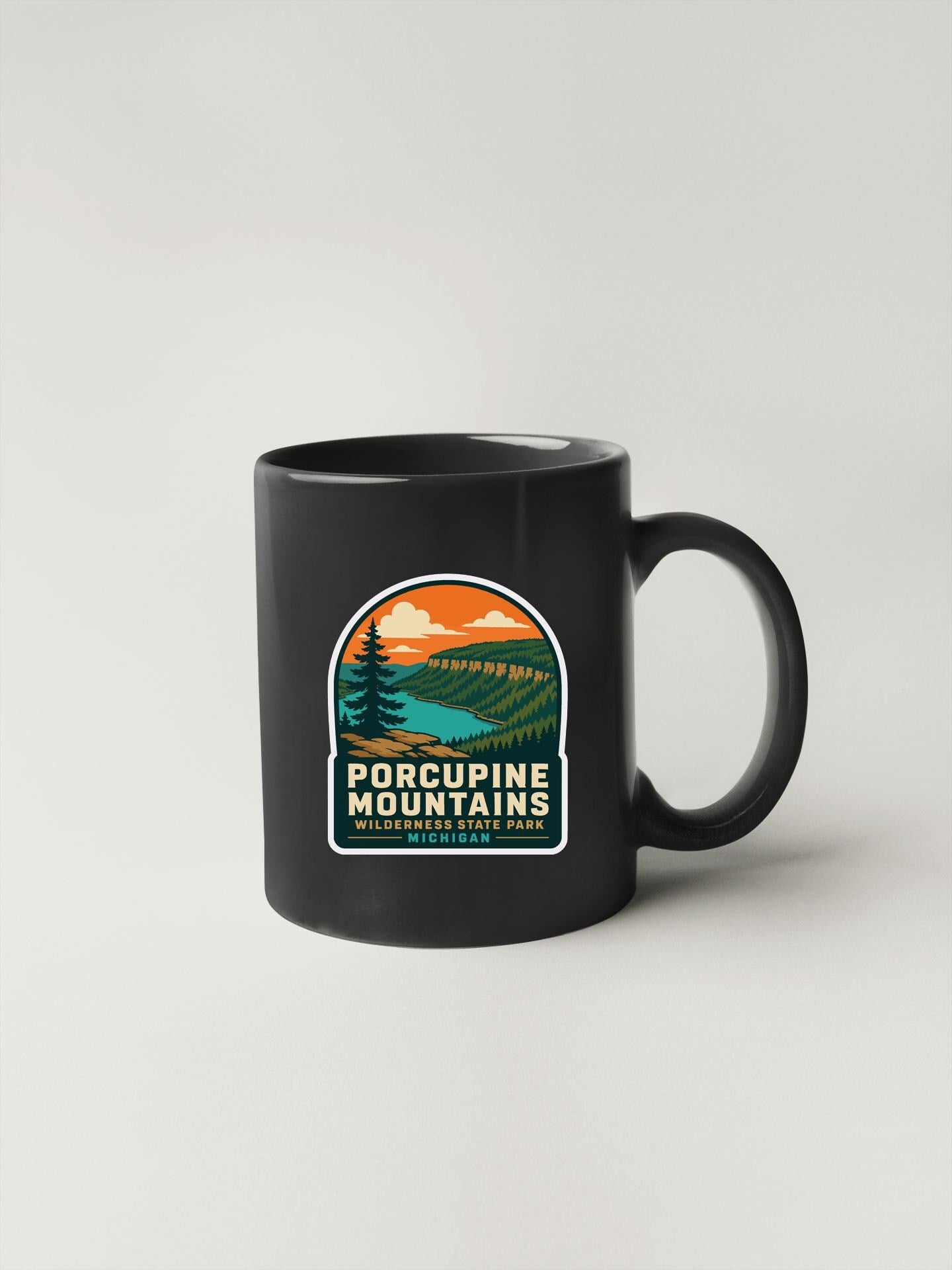 A black coffee mug with a graphic design depicting Porcupine Mountains and a sunset landscape.