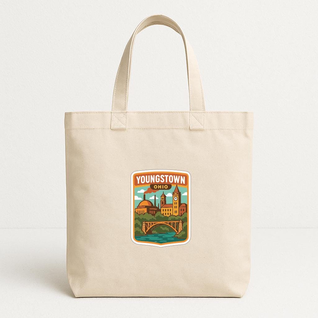 A beige tote bag with a printed sticker depicting a cityscape and the text "YOUNGSTOWN, OHIO" printed on it.