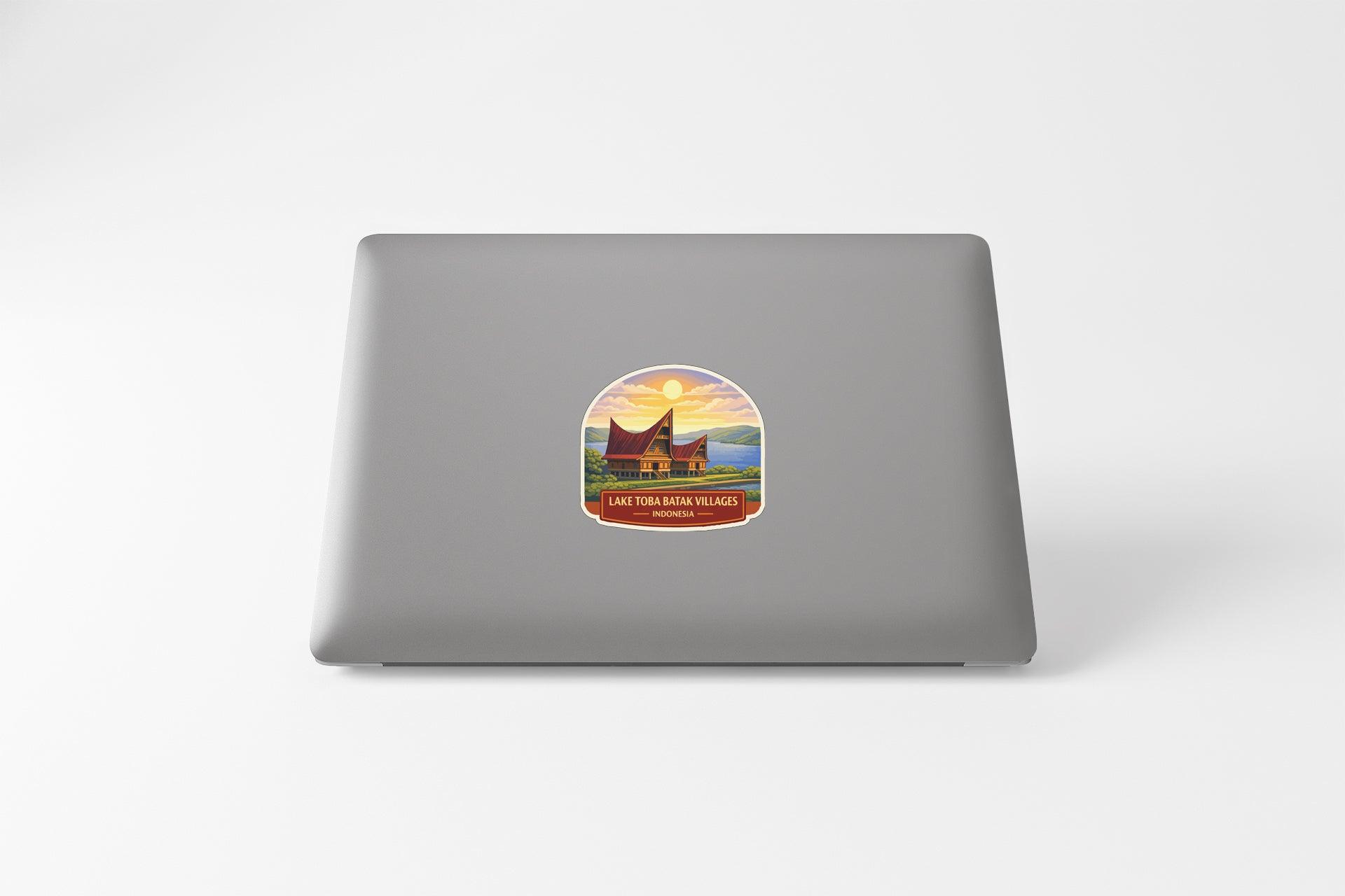 A sticker on the back of a laptop, depicting a scenic landscape with a house and a sunset.